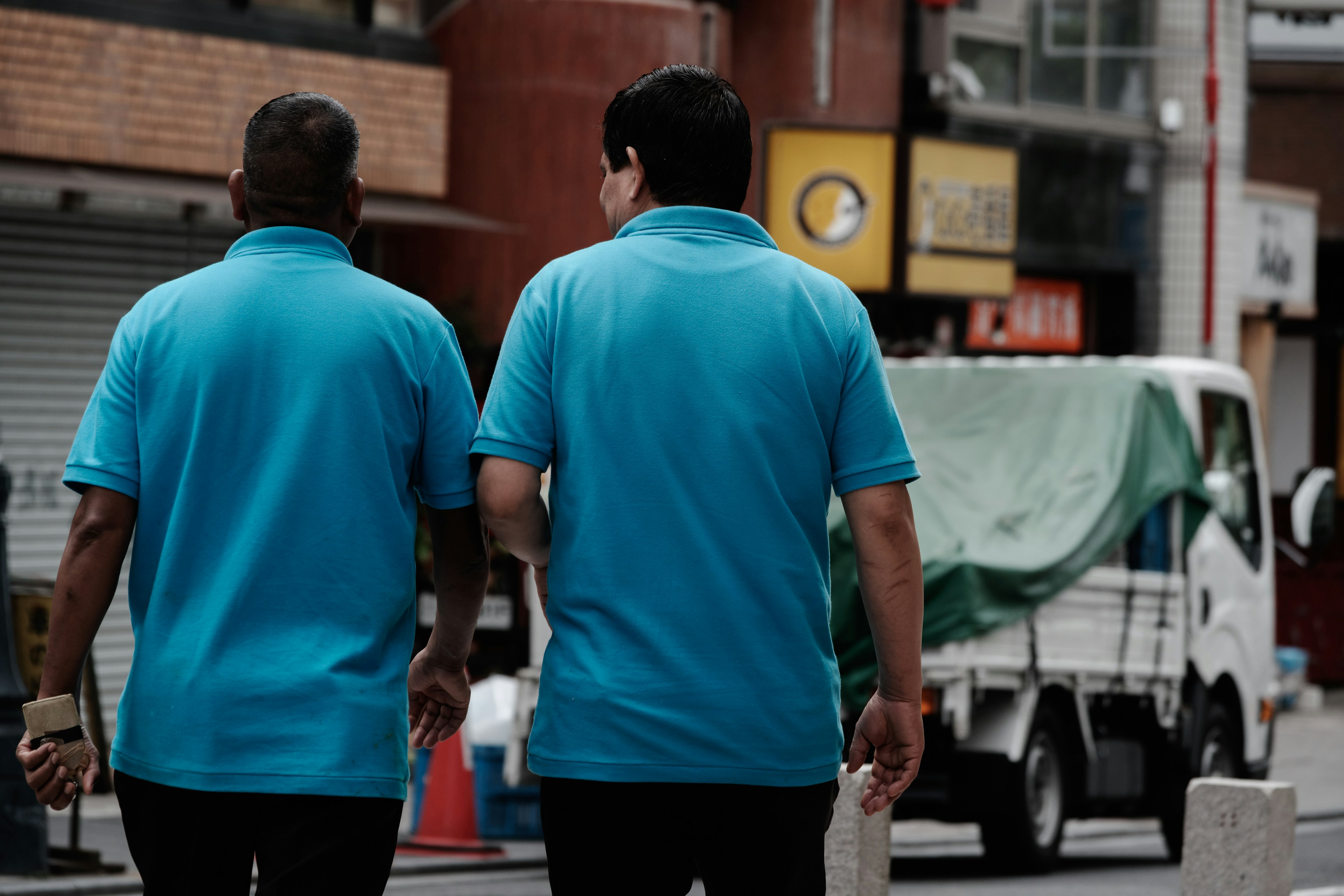 Zwei Männer in blauen Poloshirts, die in einer städtischen Umgebung gehen