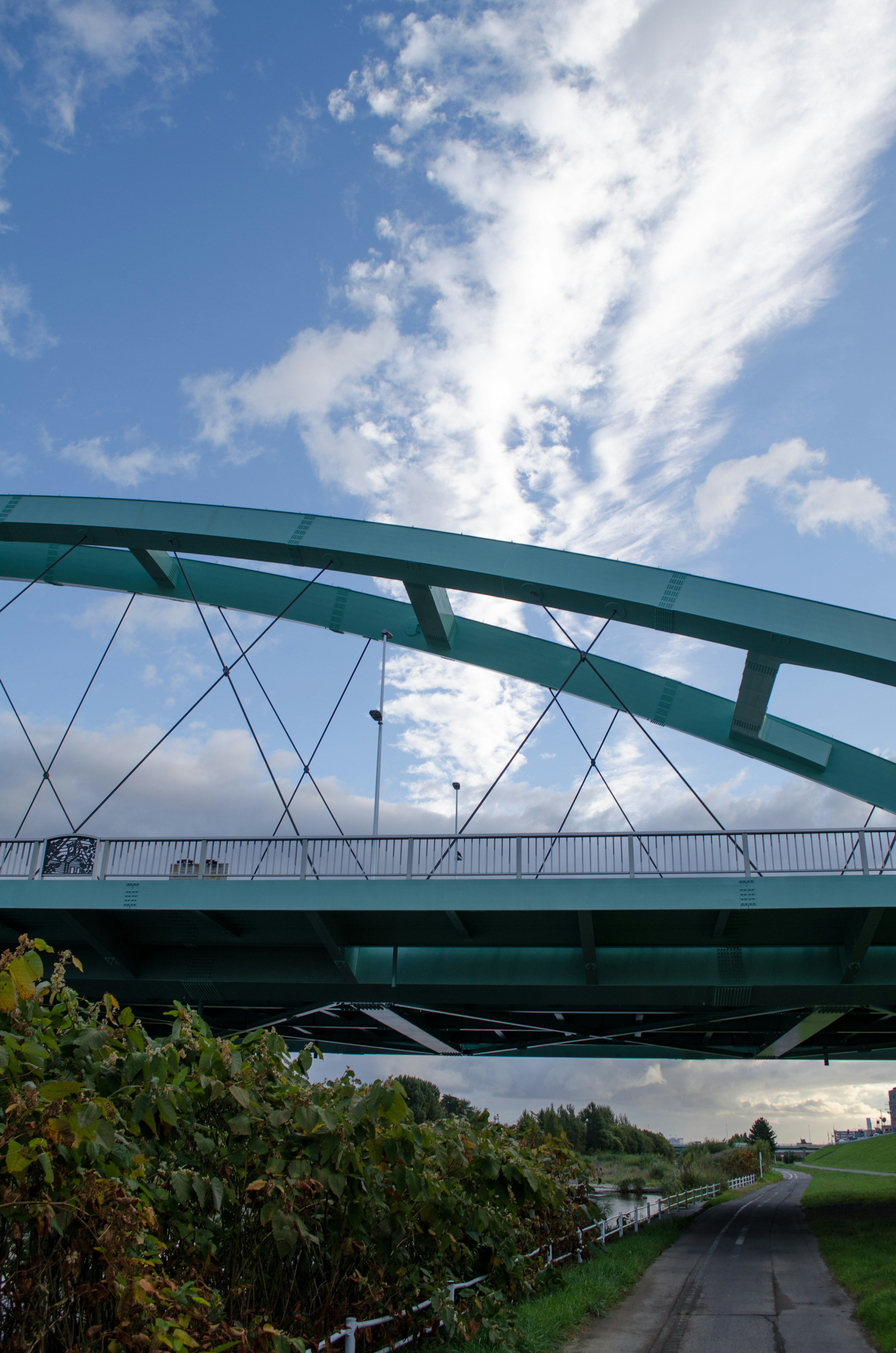 Blick von unter einer grünen Bogenbrücke mit blauem Himmel und Wolken