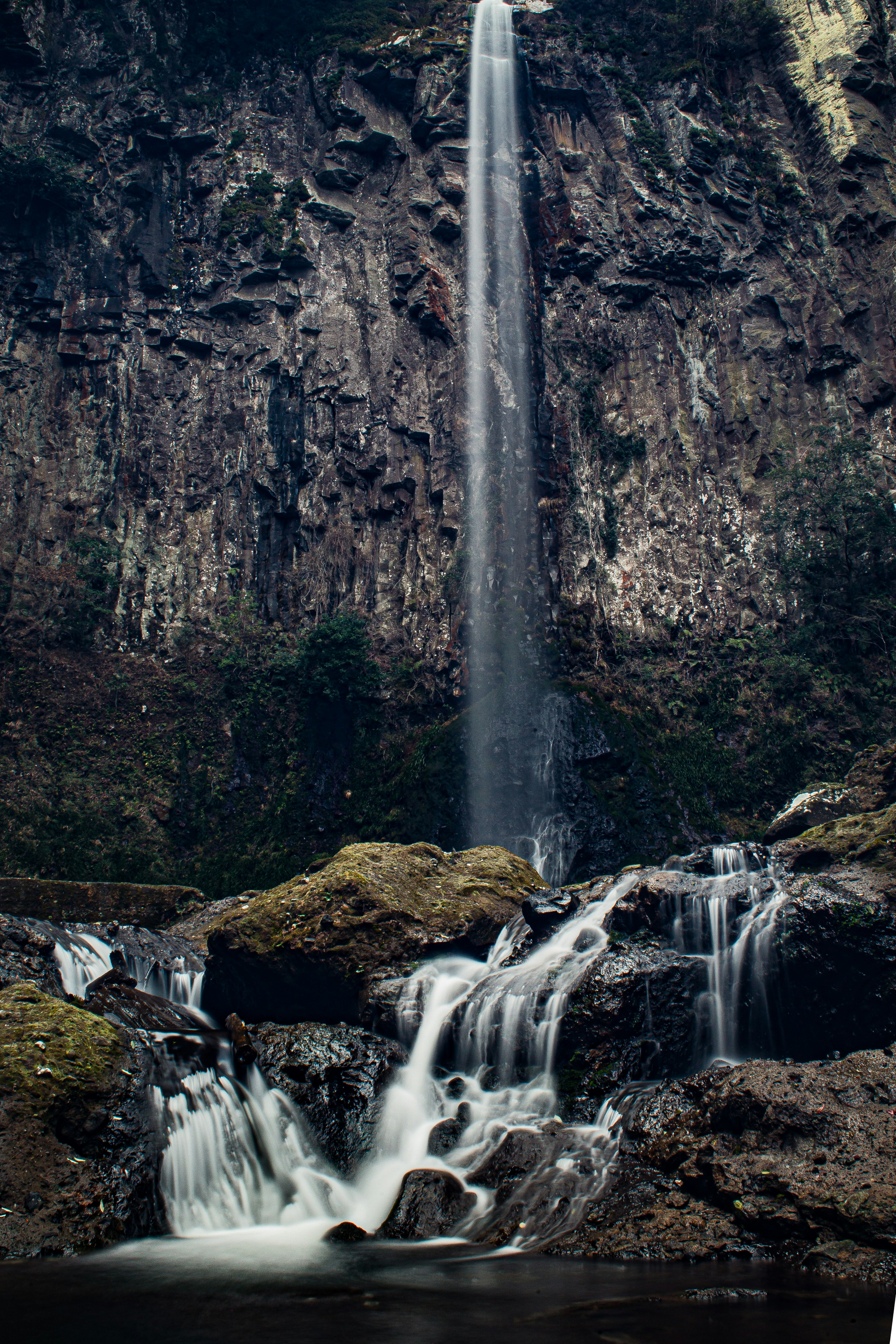 Air terjun yang indah dikelilingi oleh batu dan dedaunan hijau dalam pengaturan alami