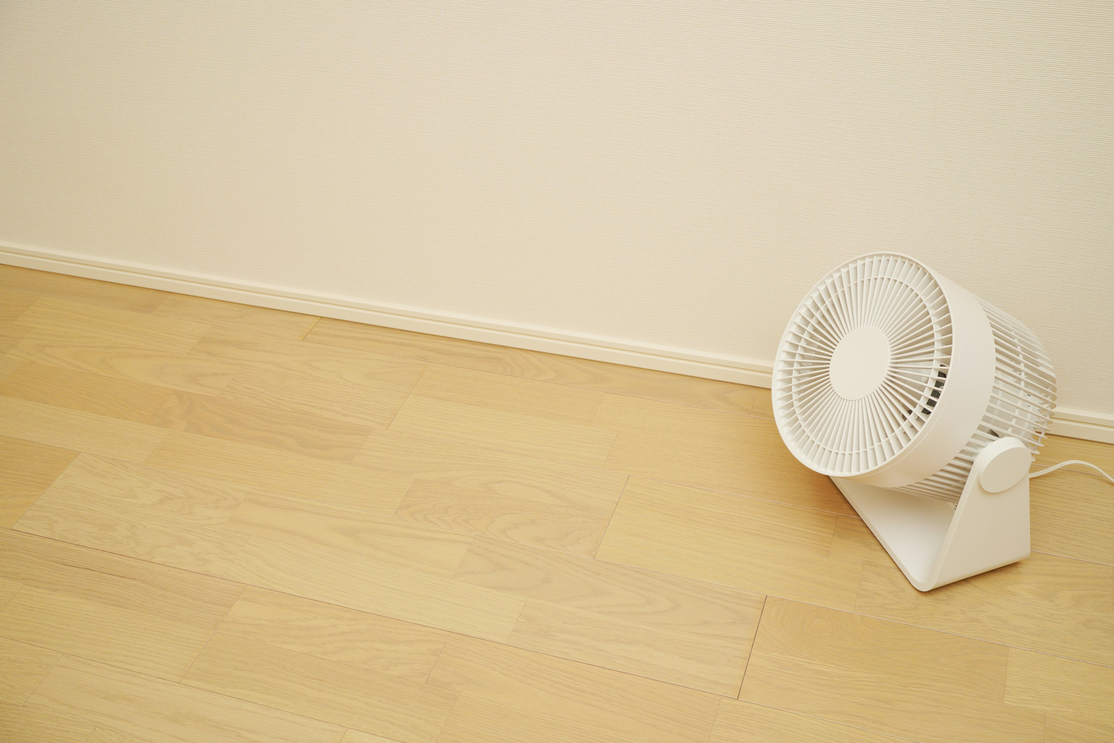 Un ventilador blanco colocado contra una pared en una habitación simple