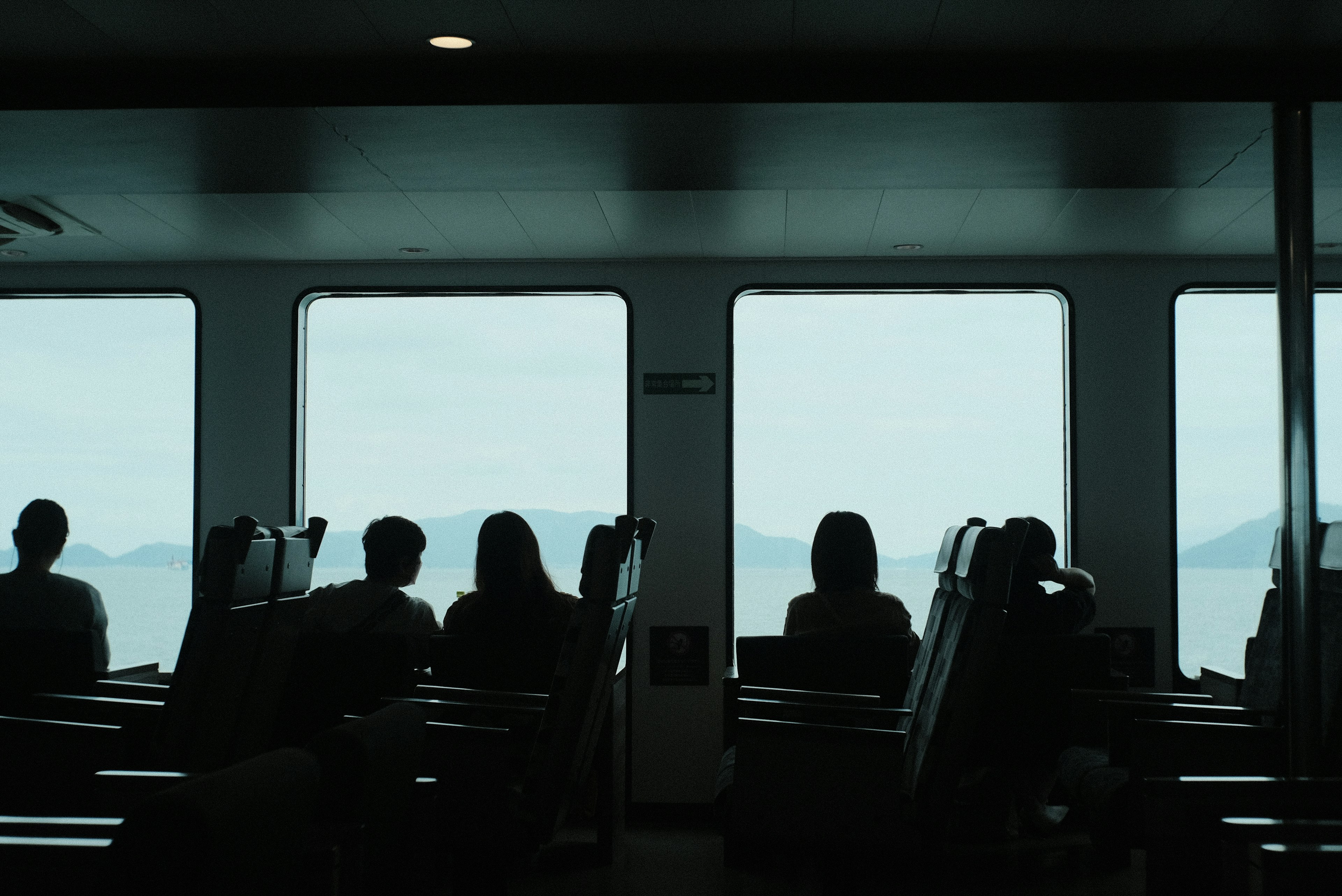 Silhouettes of people looking out at the sea and mountains through windows