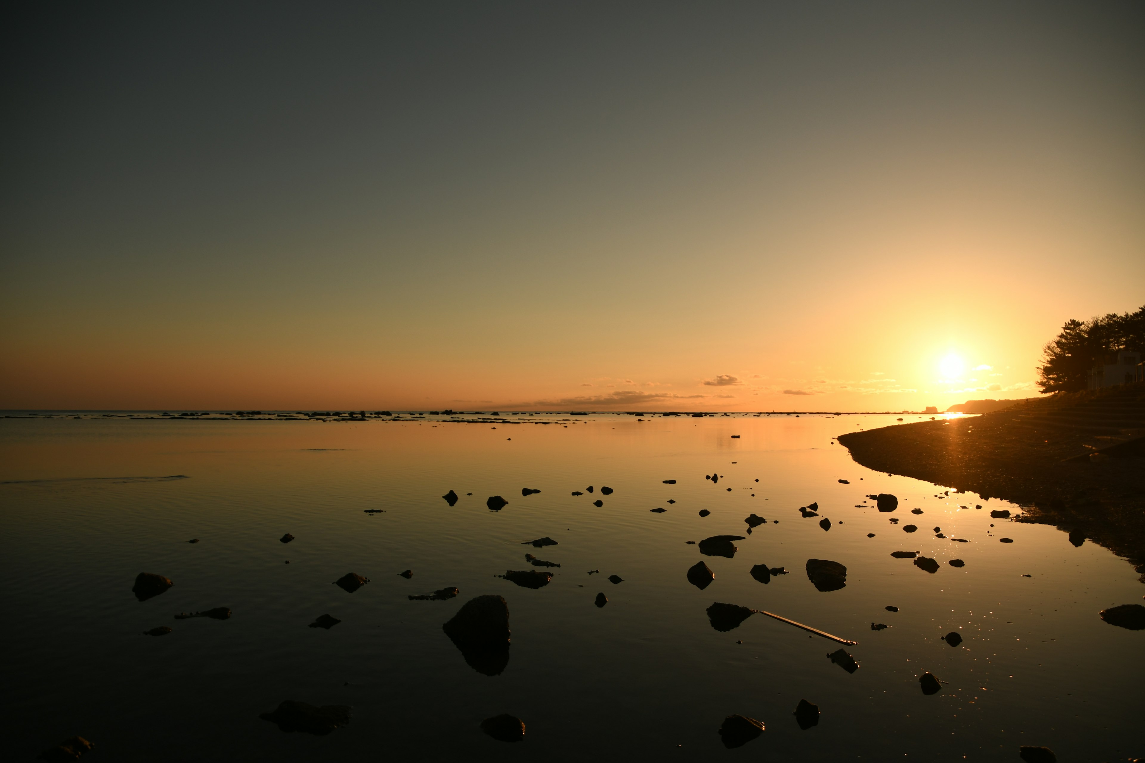 Ruhige Küste mit einem Sonnenuntergang, der sich auf einer ruhigen Wasseroberfläche spiegelt