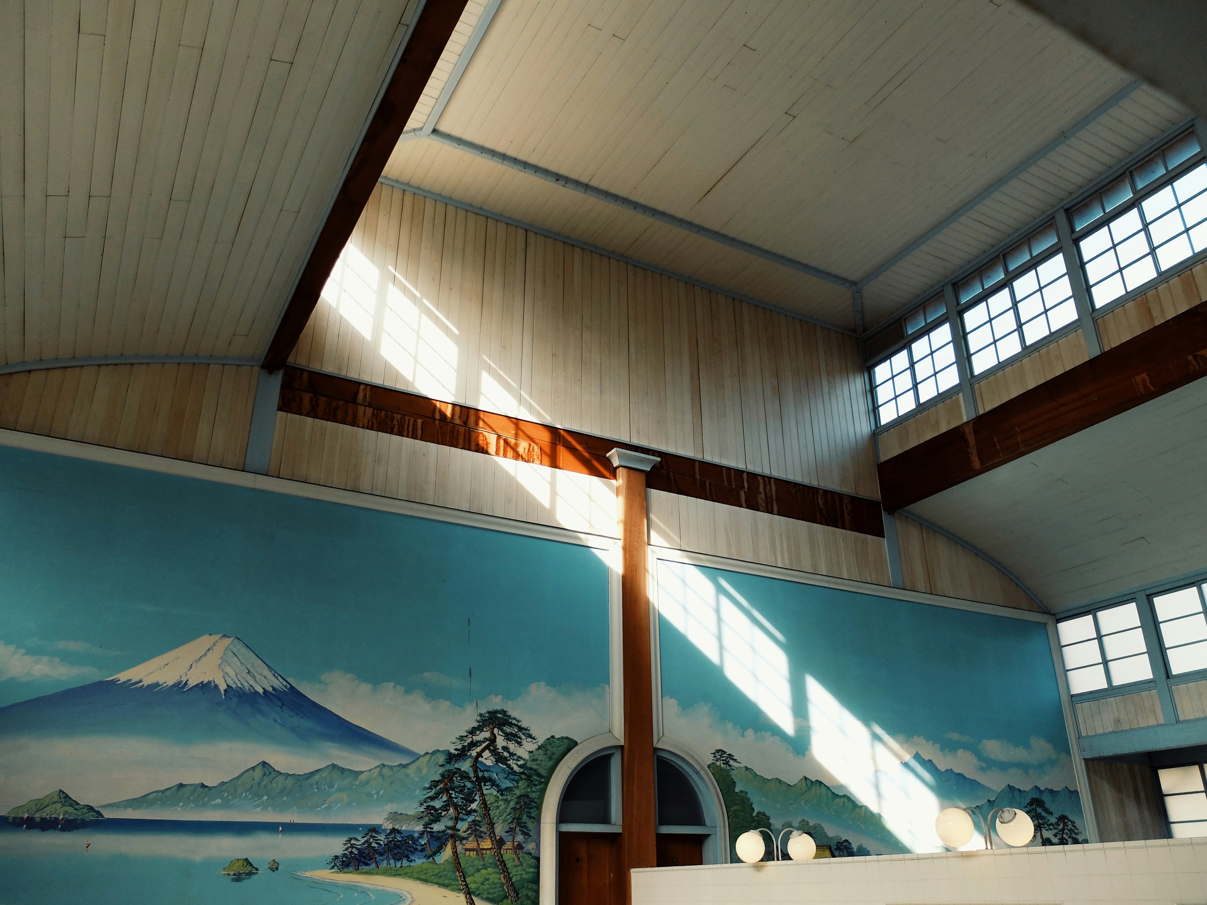 Intérieur d'une pièce avec de grandes fenêtres et de la lumière du soleil entrant mettant en avant une fresque du mont Fuji