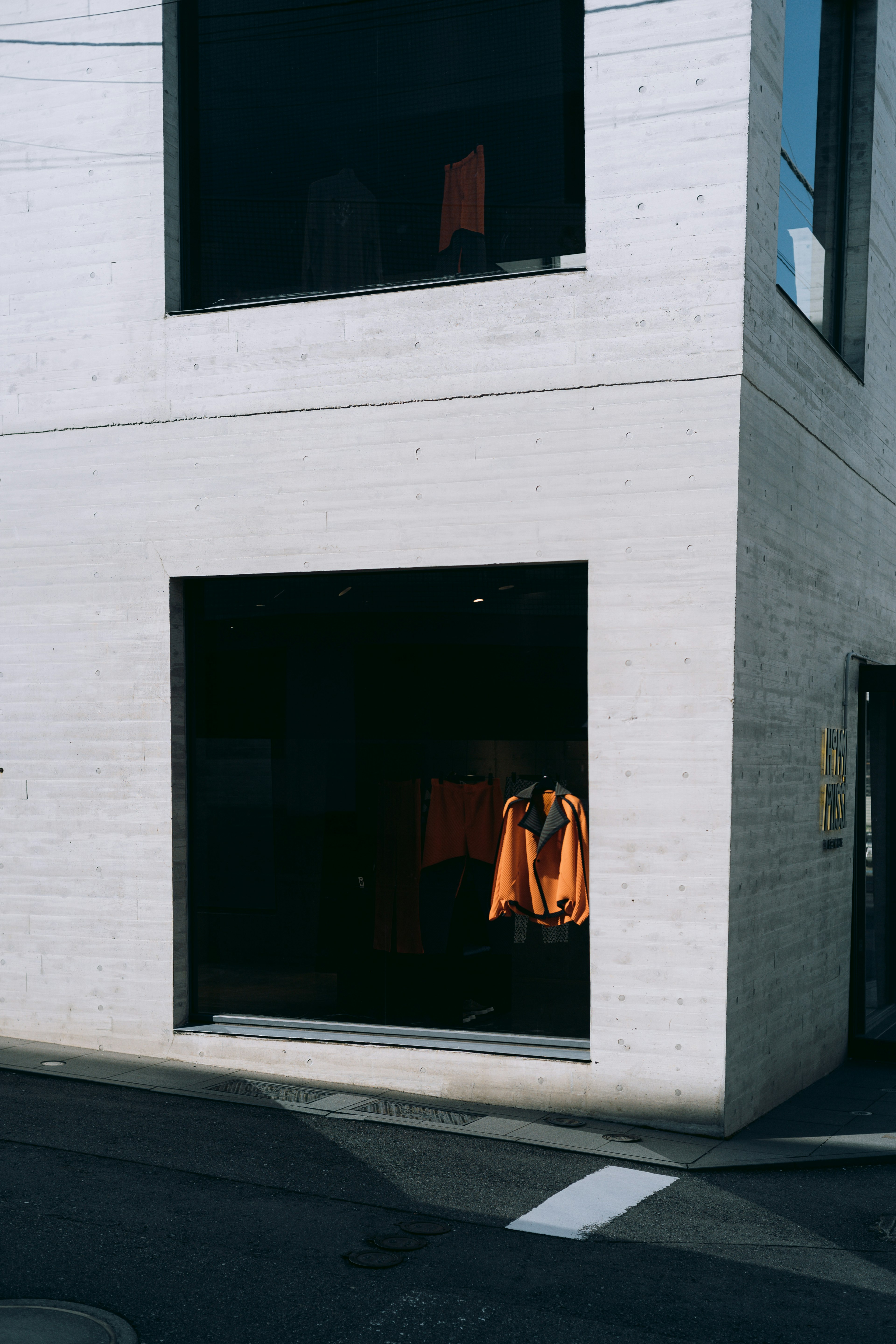 A corner store with a white exterior and large windows showcasing orange clothing