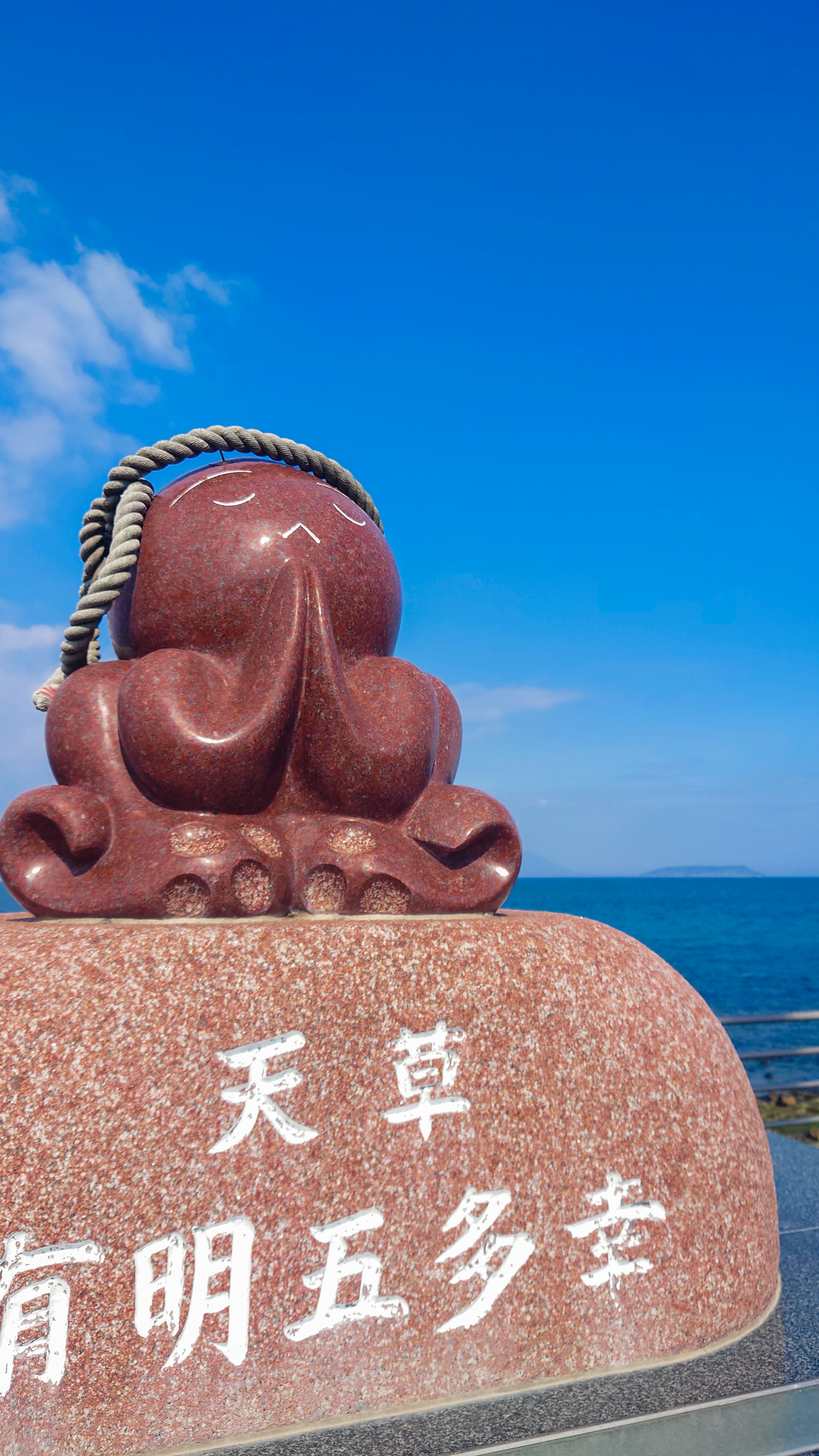 A reddish stone sculpture of a sitting octopus under a blue sky