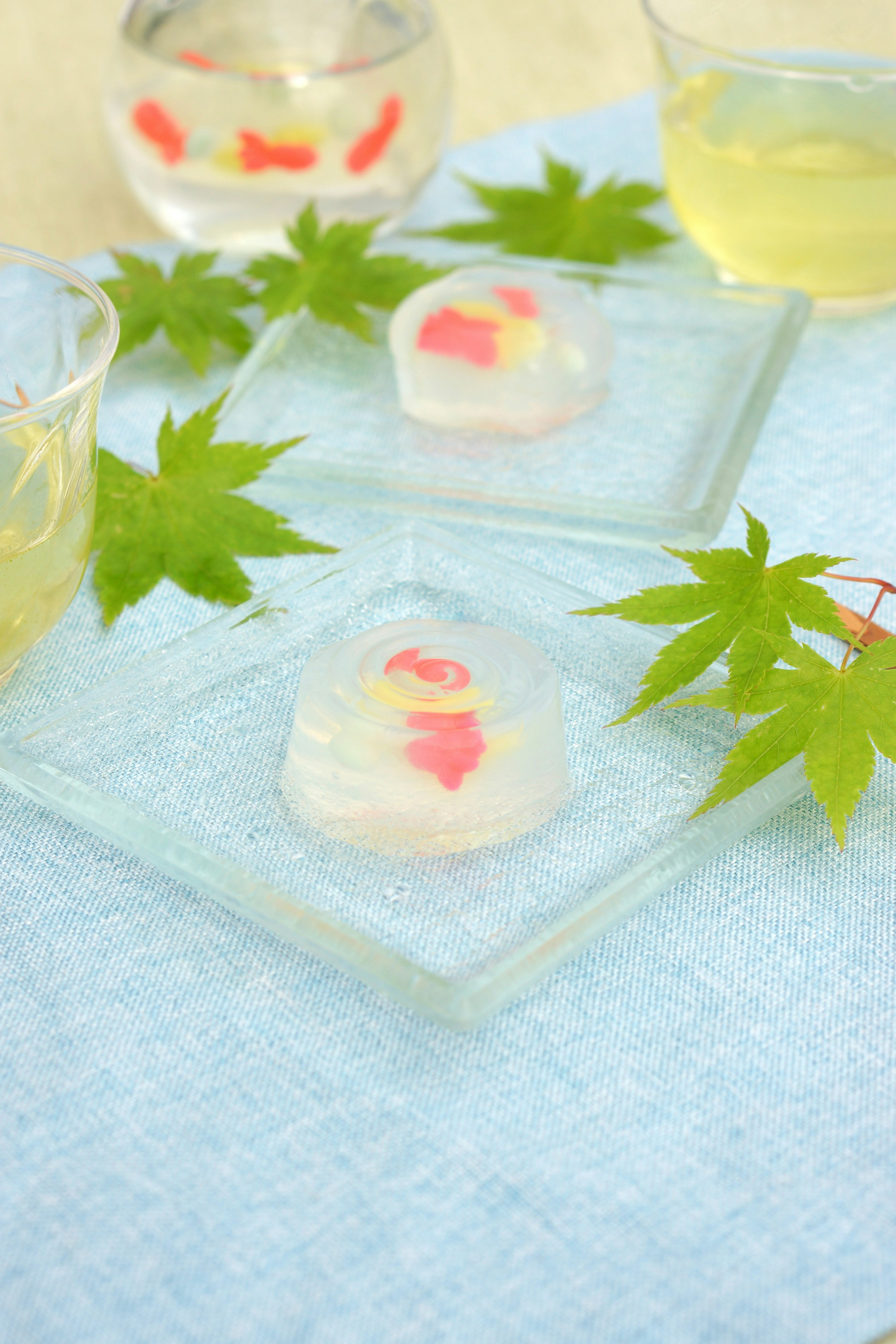 Transparent Japanese sweets with colorful flower designs and green maple leaves on a light blue table