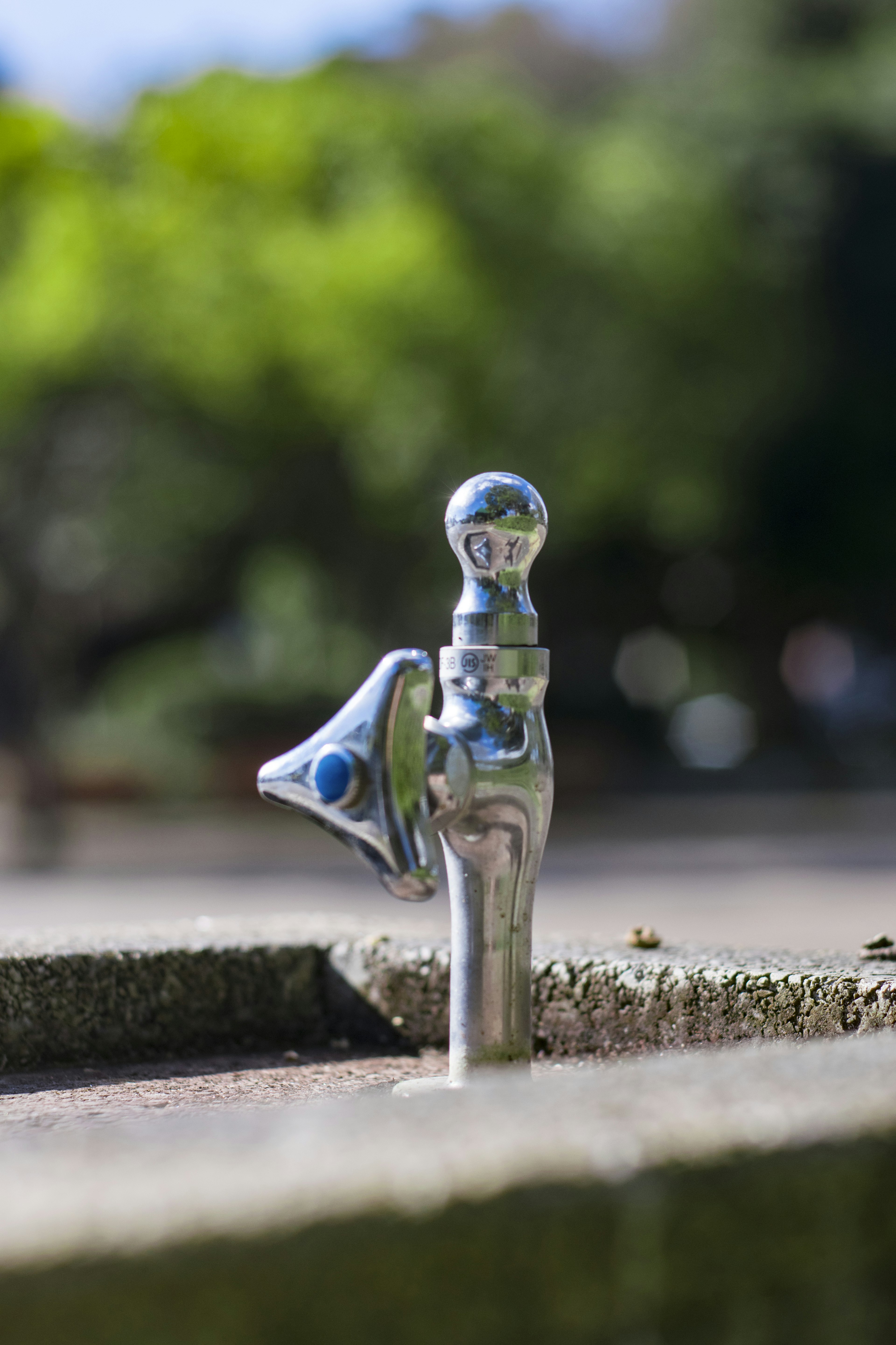 Metallener Wasserbrunnen mit blauem Auslauf in einem Park