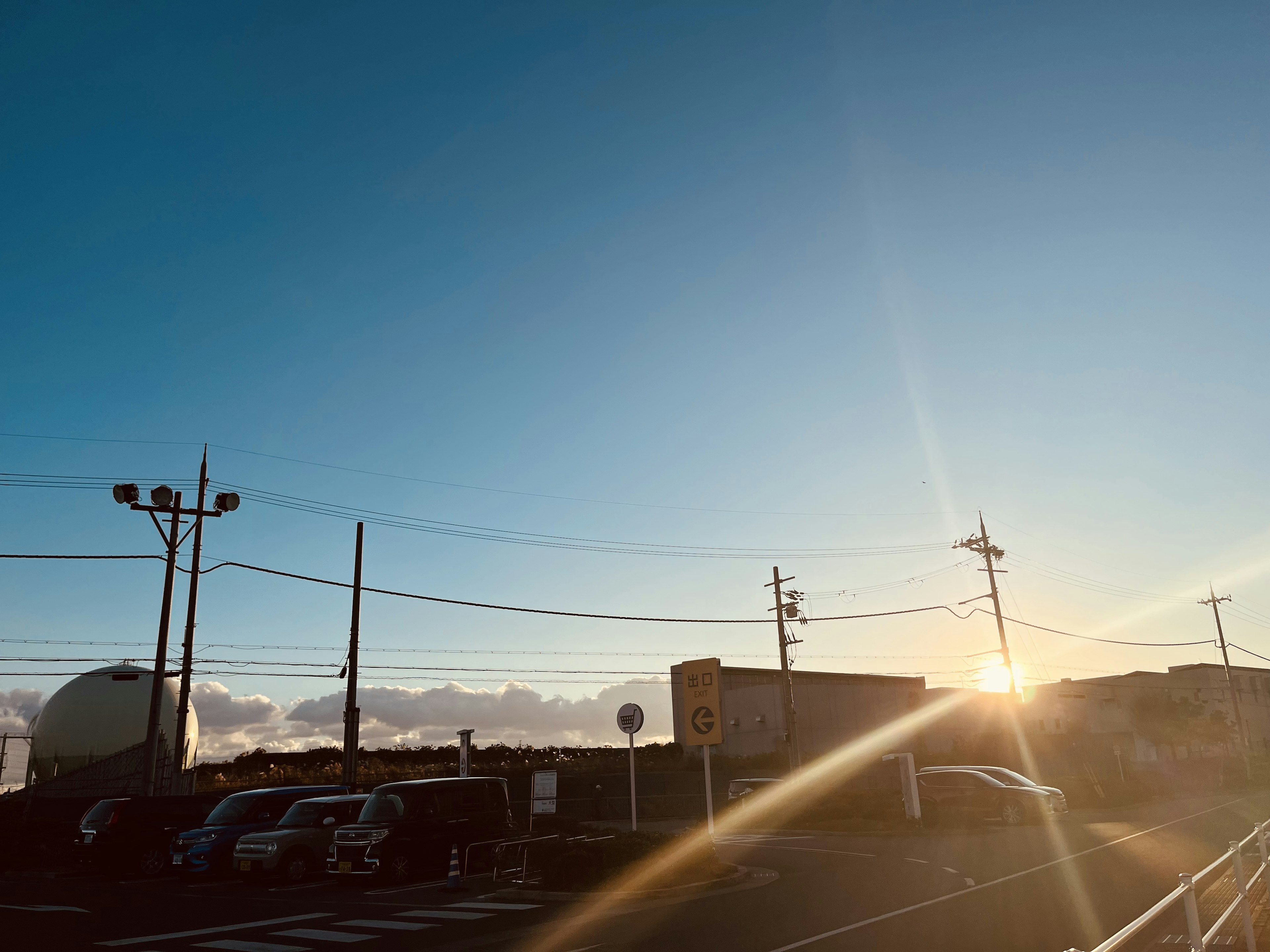 青空の下での夕日が沈む風景 車が並んでいる駐車場と電柱が見える