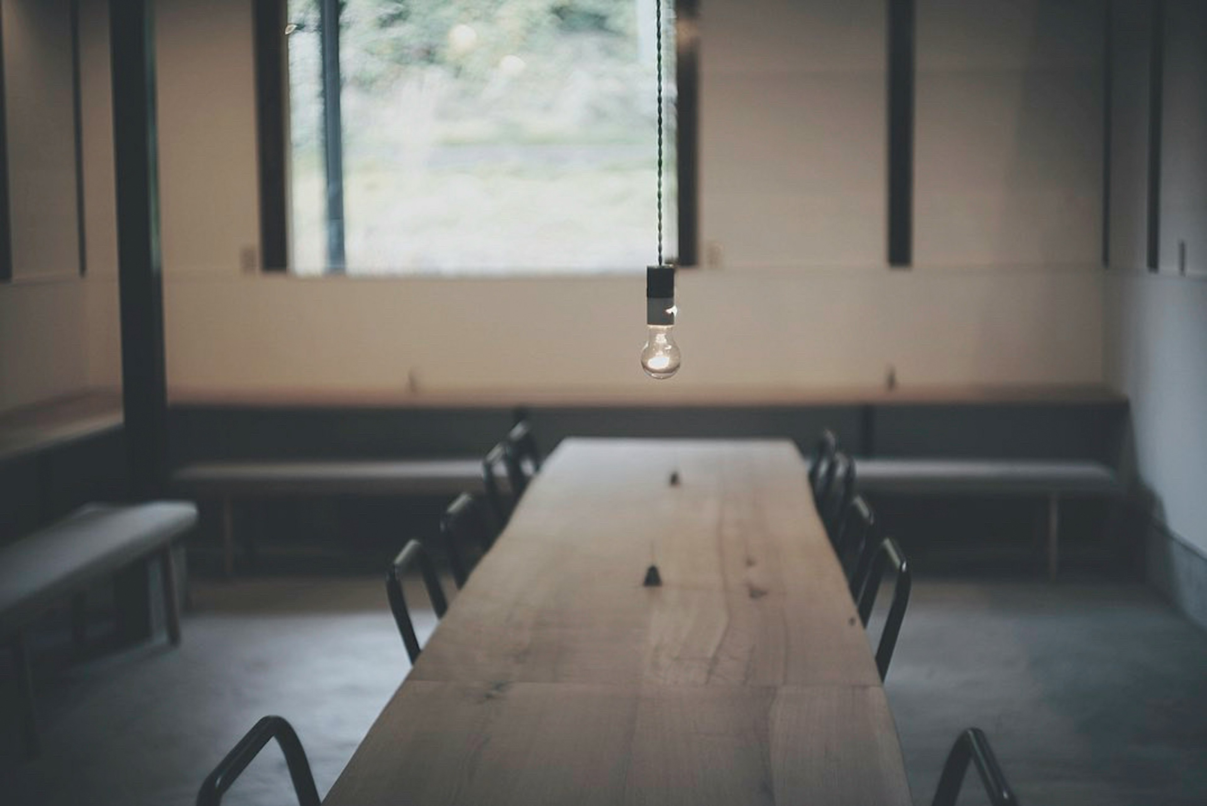 Simple modern meeting room interior featuring a wooden long table and black chairs Natural light streaming through a large window