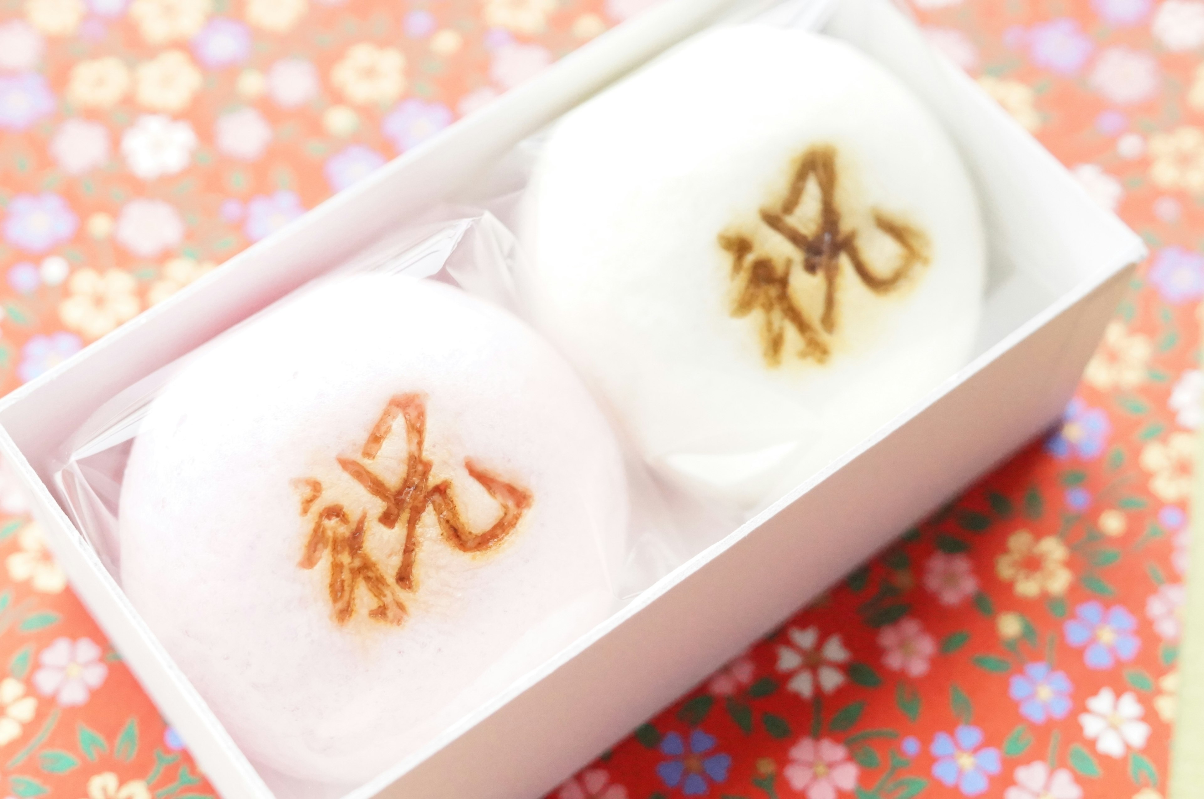 Une boîte contenant des wagashi blancs et roses avec le caractère de célébration visible