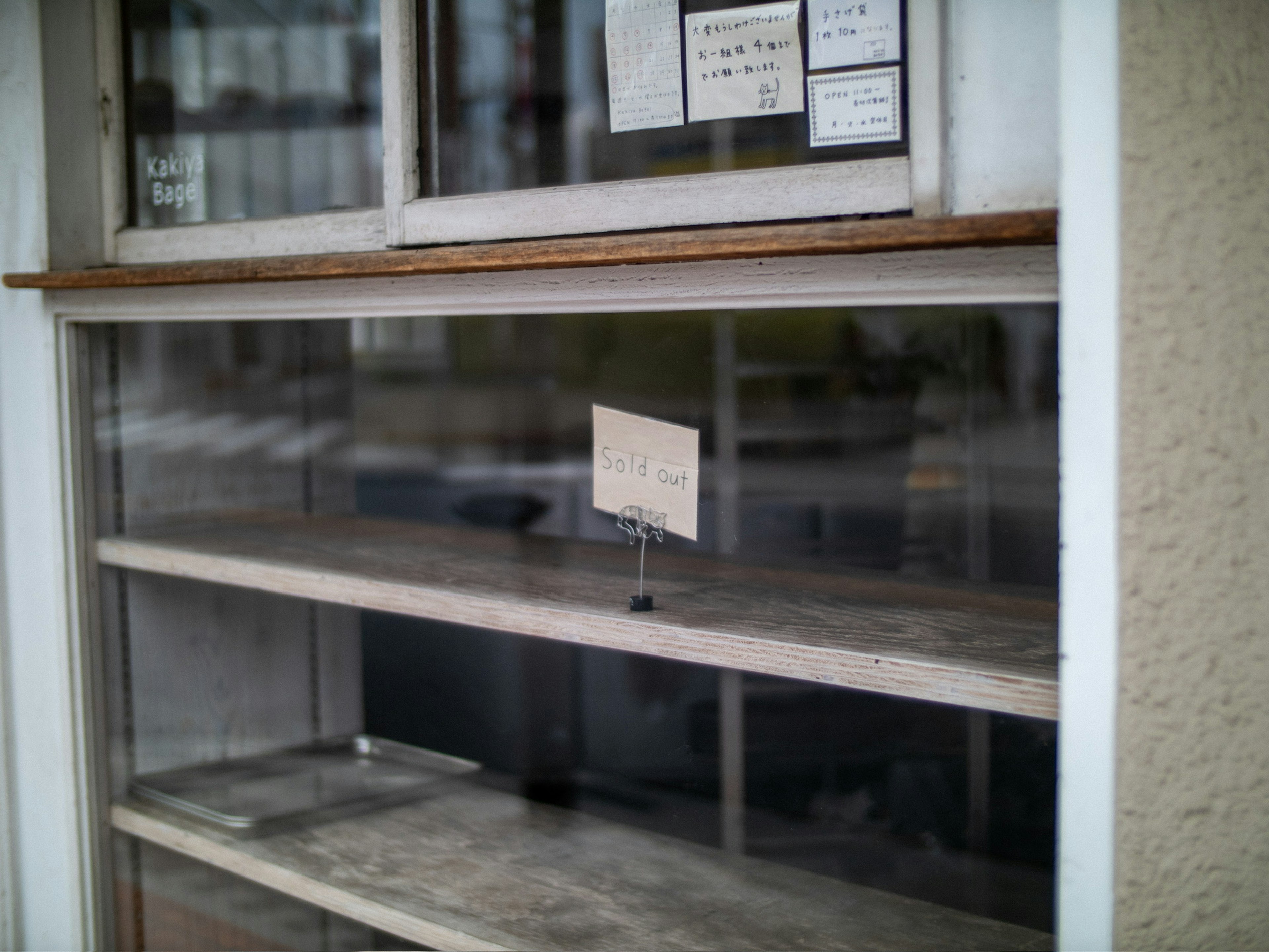 Empty shelves visible through a glass window with handwritten signs