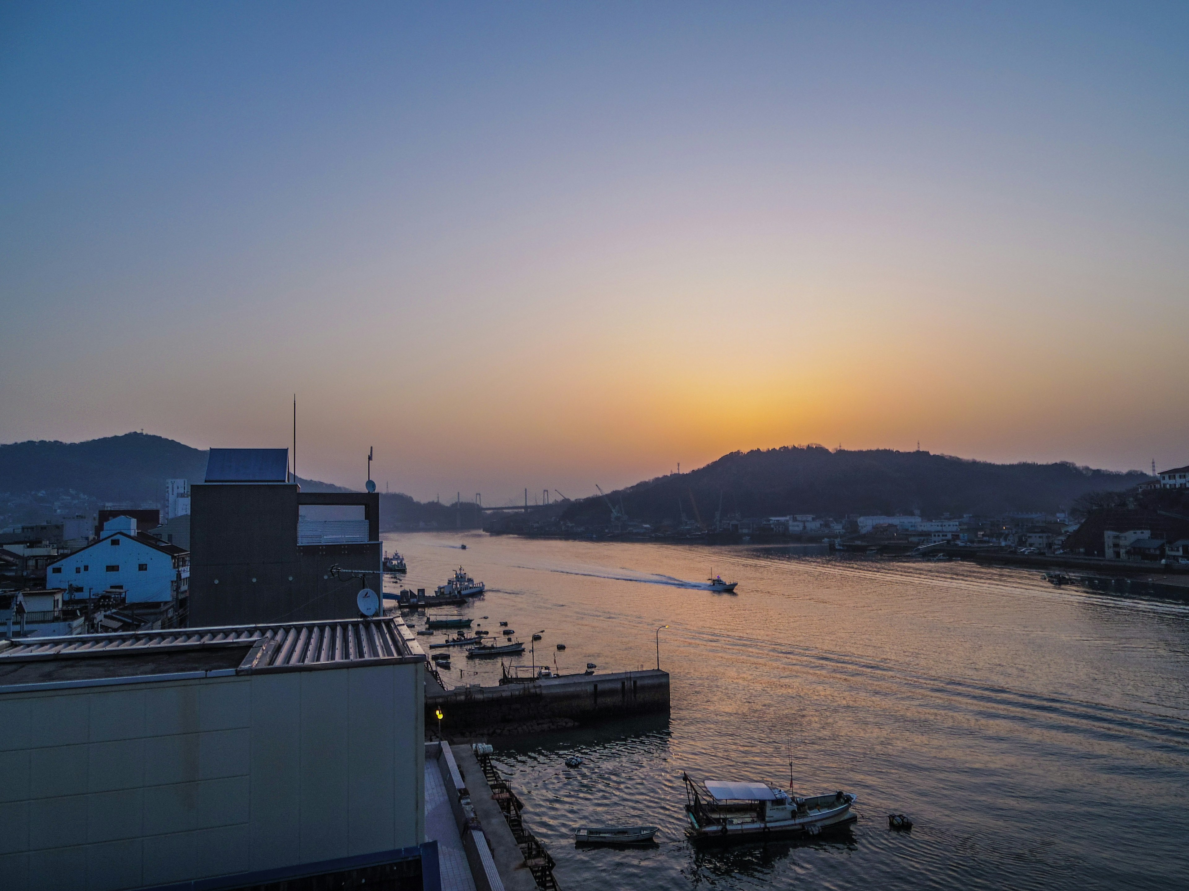 Vista del atardecer sobre un río con barcos y colinas al fondo