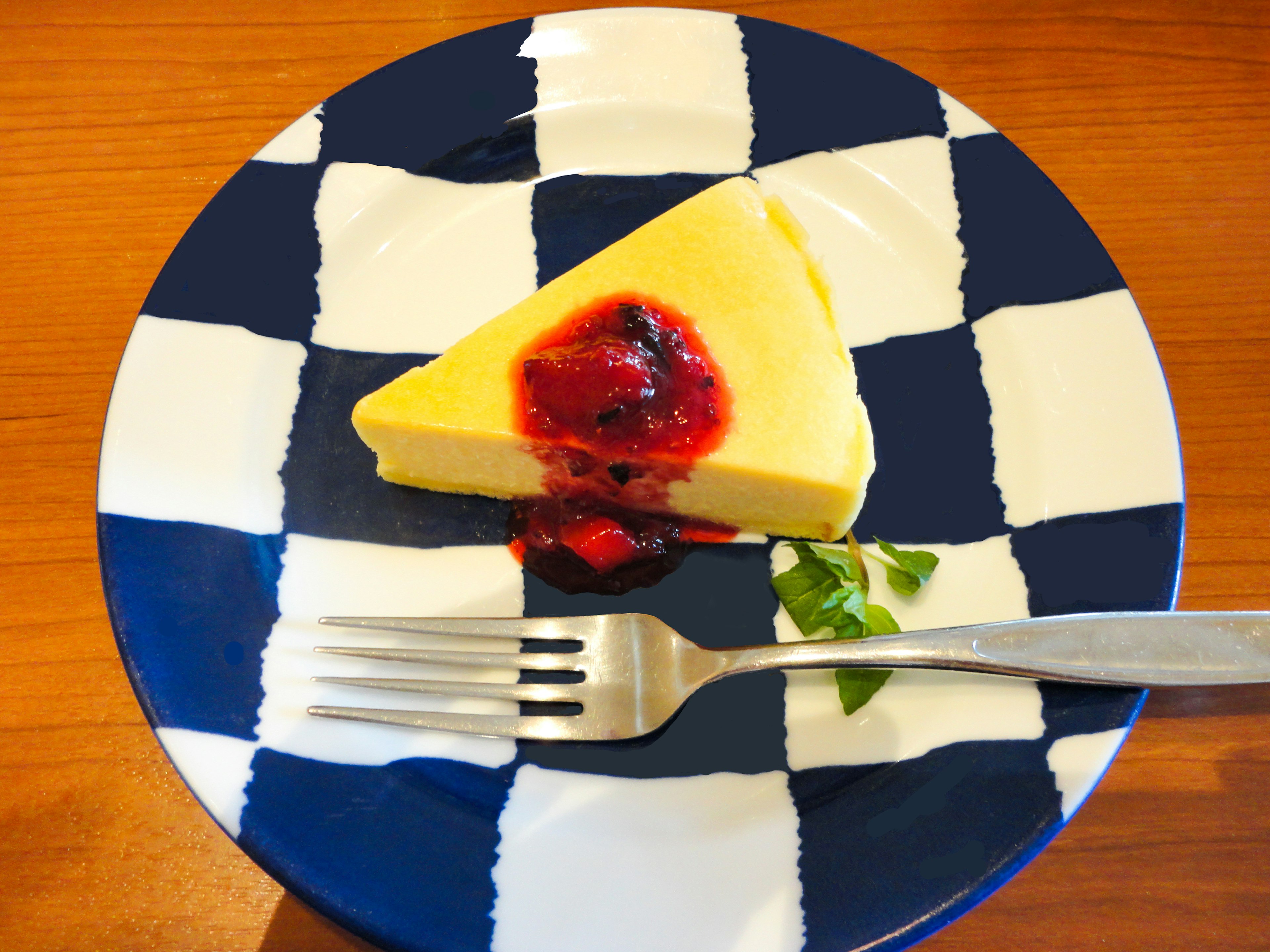 Stück Käsekuchen mit Beerensauce auf einem blau-weißen karierten Teller