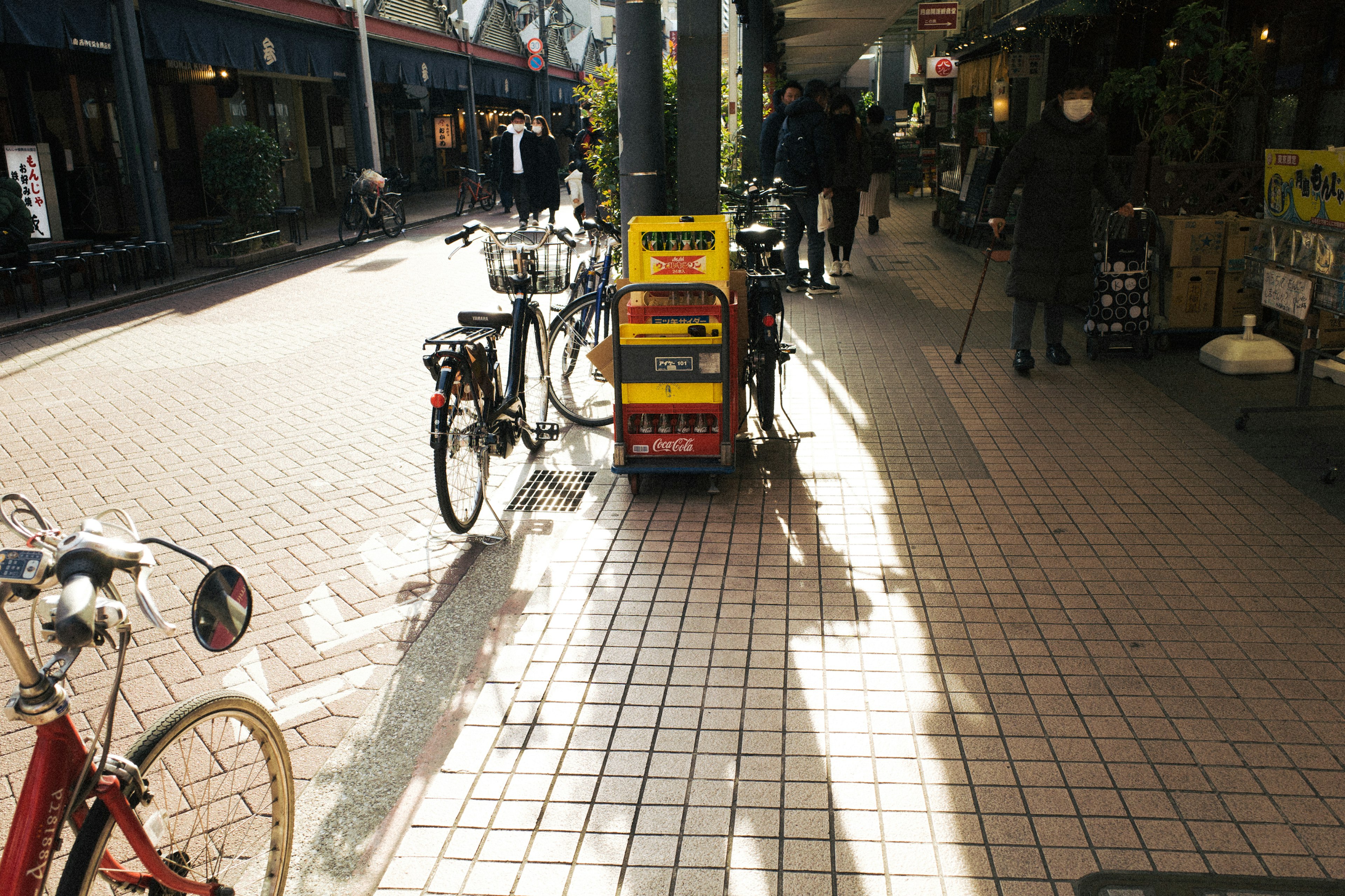 自転車が並ぶ賑やかな商店街の一角で、日差しが差し込むタイルの道