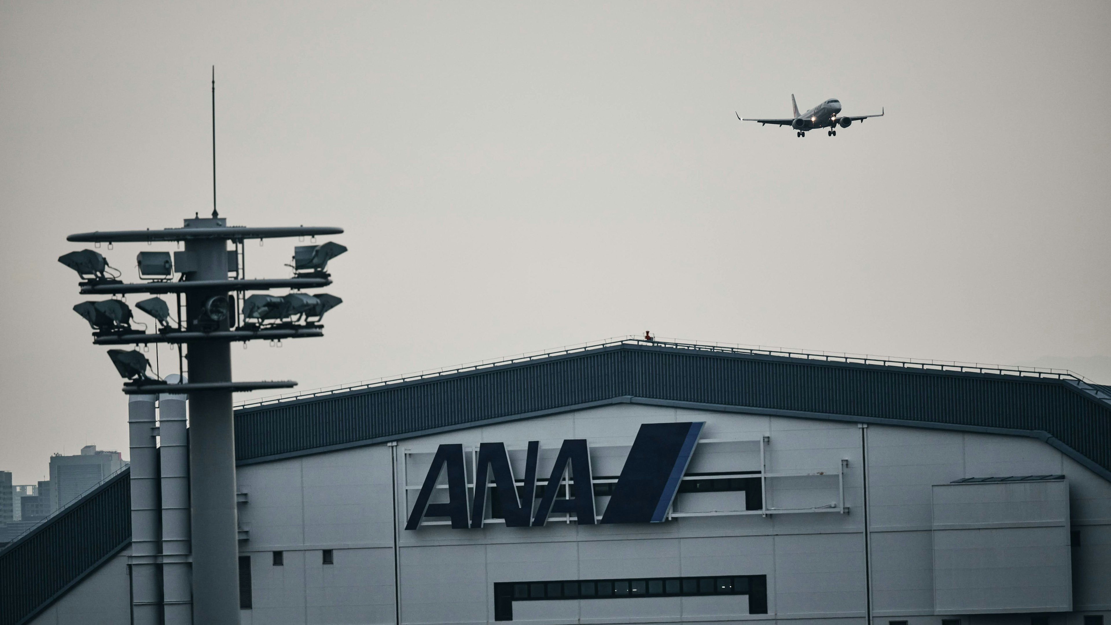 Logo ANA terlihat di gedung bandara dengan pesawat yang mendekat