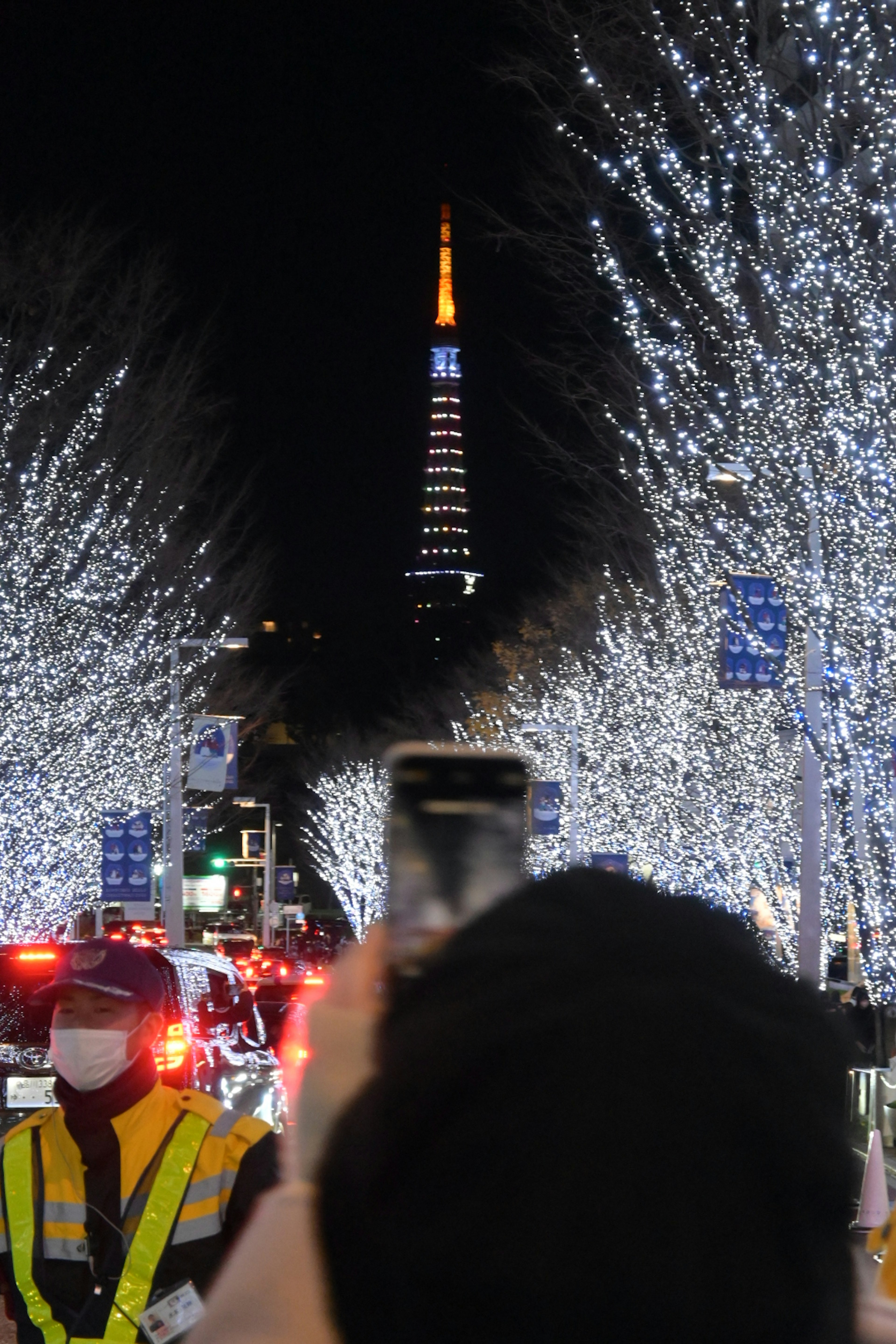 Una persona capturando la torre de Tokio iluminada en una calle bordeada de luces brillantes