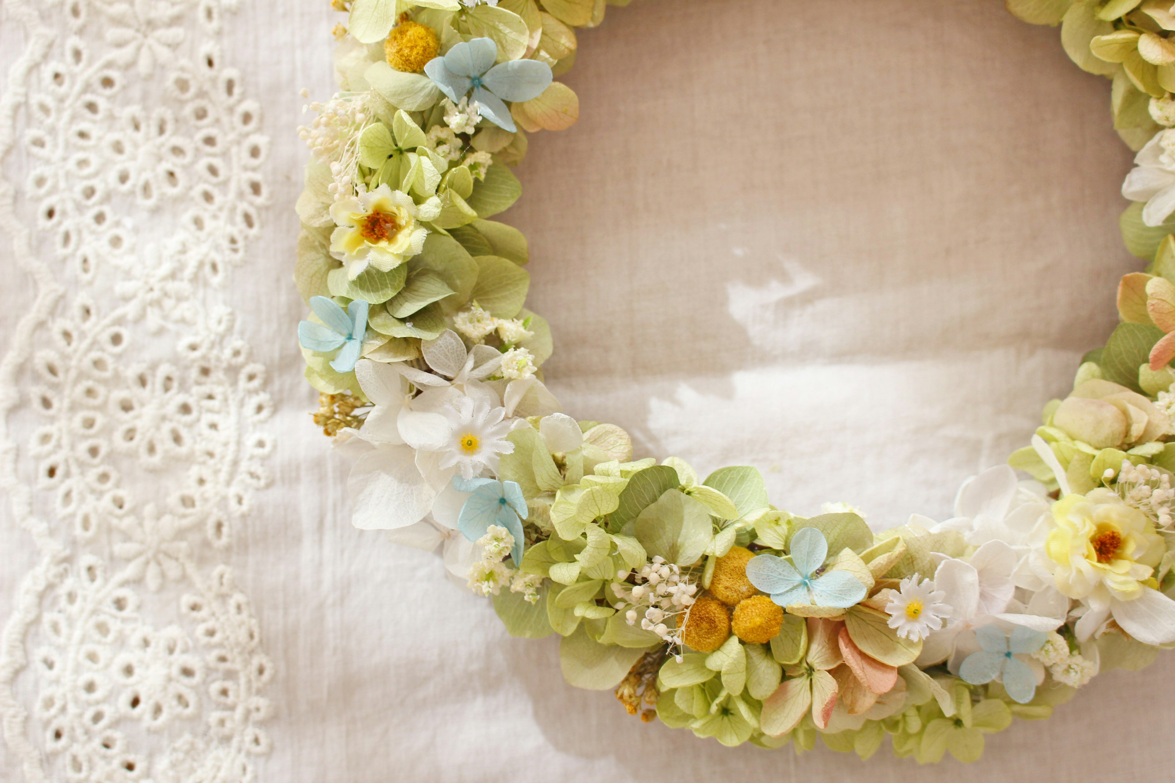 A green wreath adorned with pastel flowers resting on a white fabric