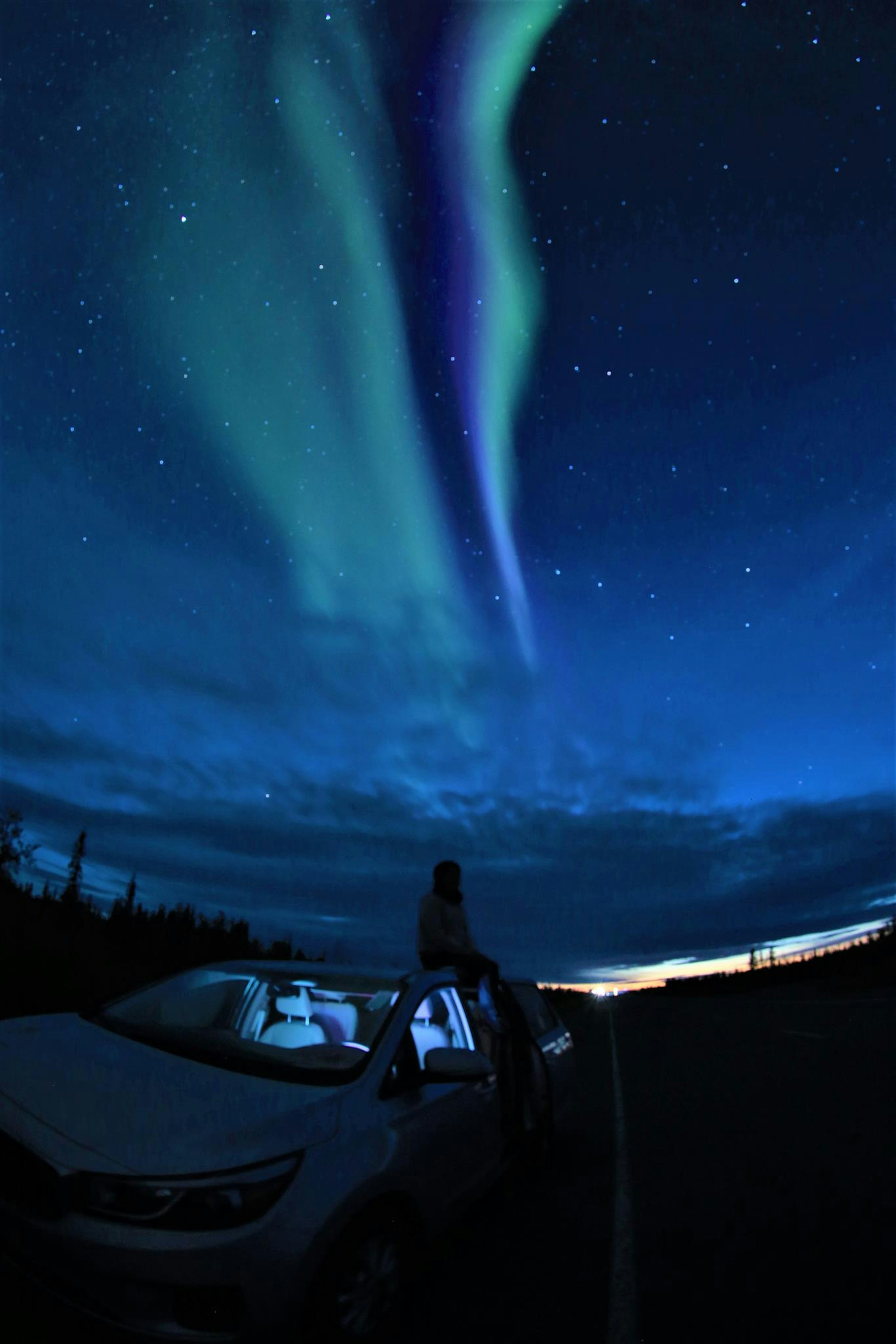 Person standing on a car under a vibrant aurora in a starry sky