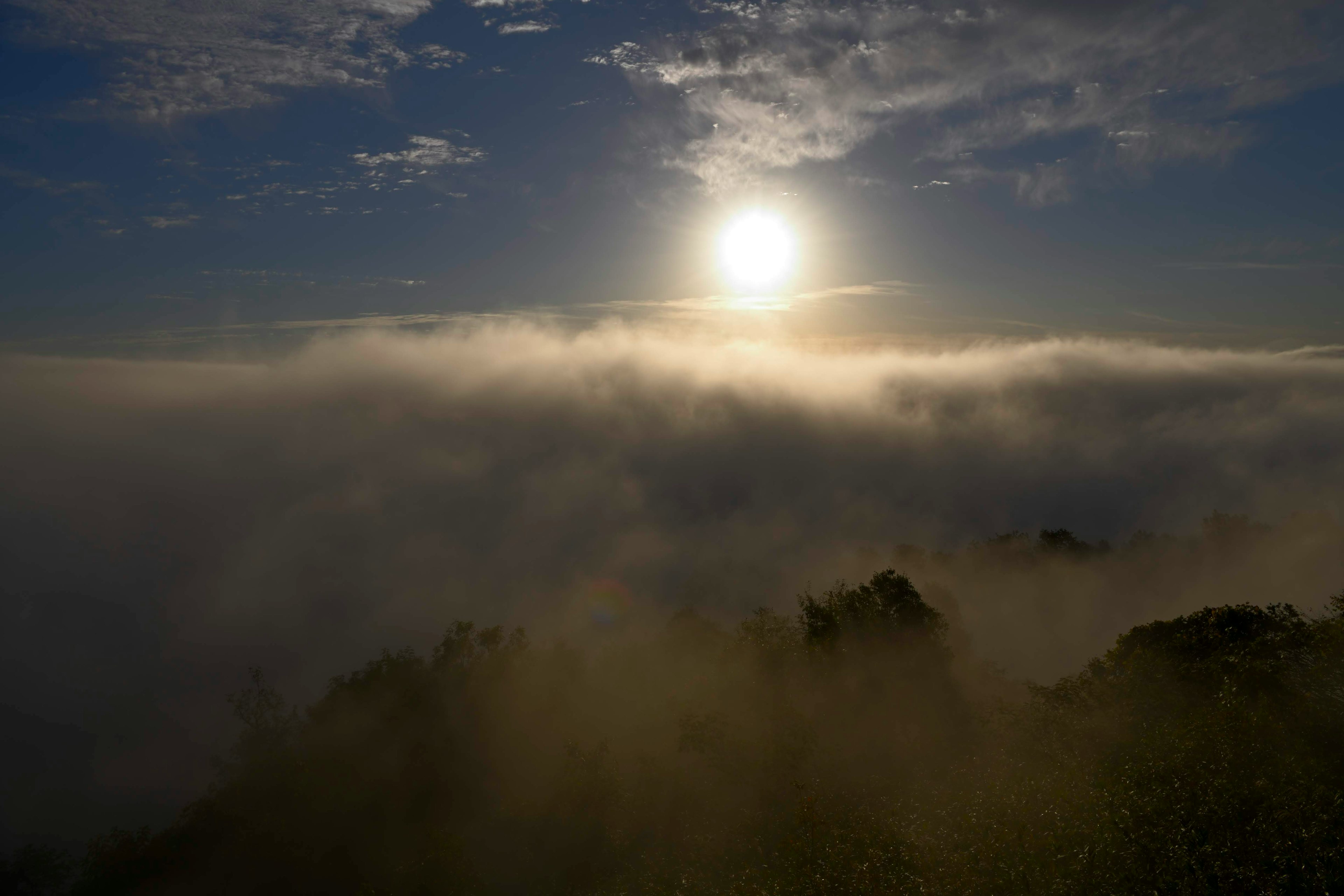 Sun rising above a misty landscape with clouds