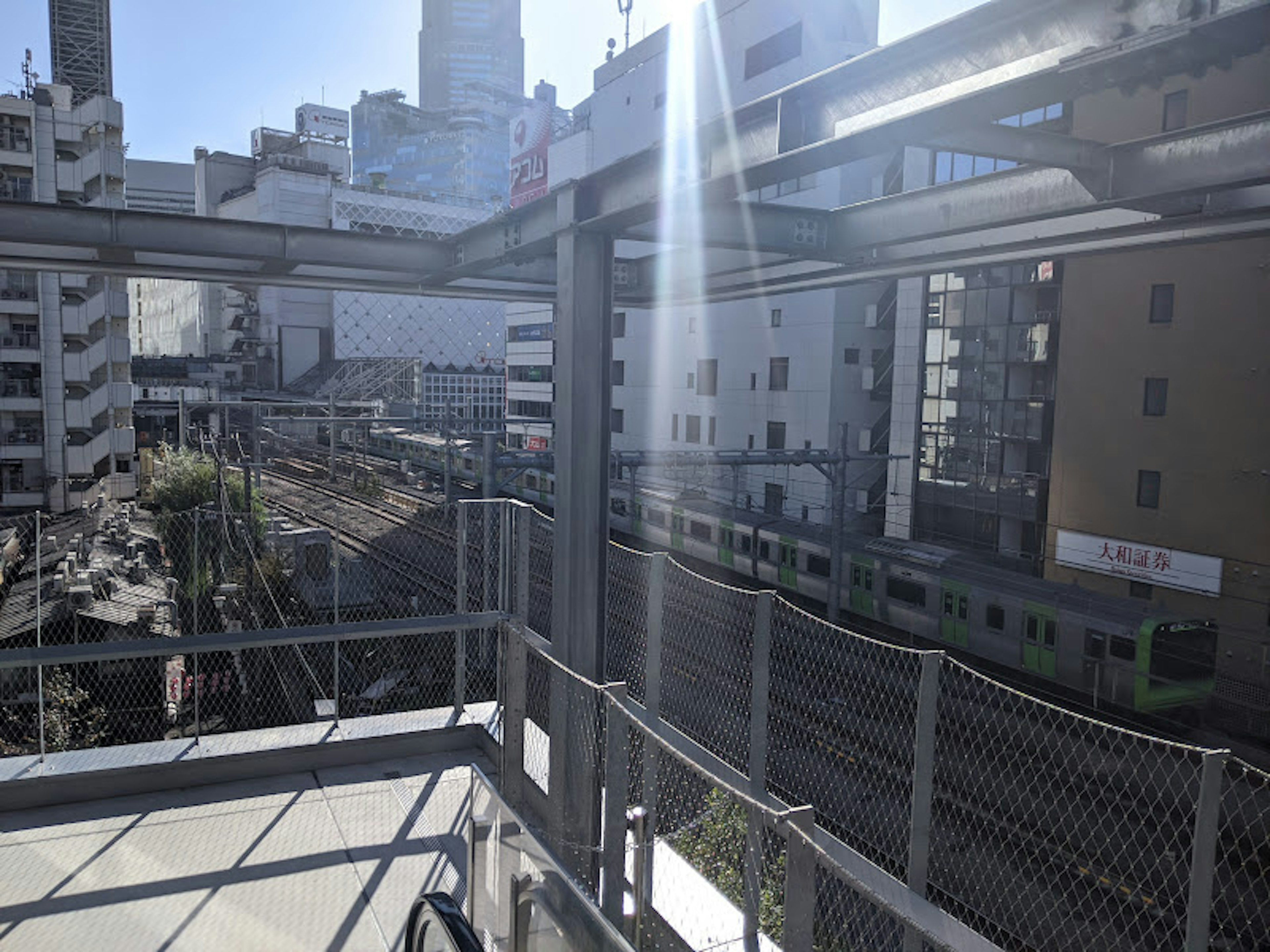 View from a construction site overlooking tall buildings and train tracks under sunlight