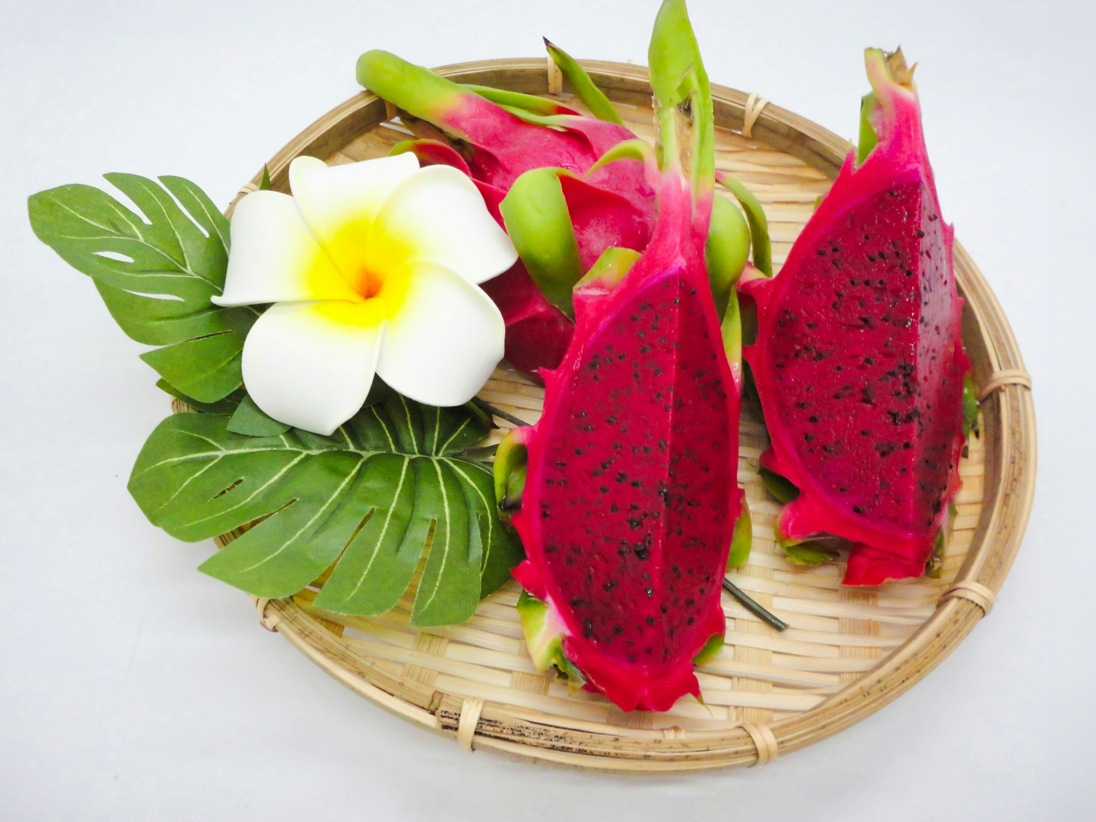 Colorful dragon fruit slices with a white flower on a bamboo plate