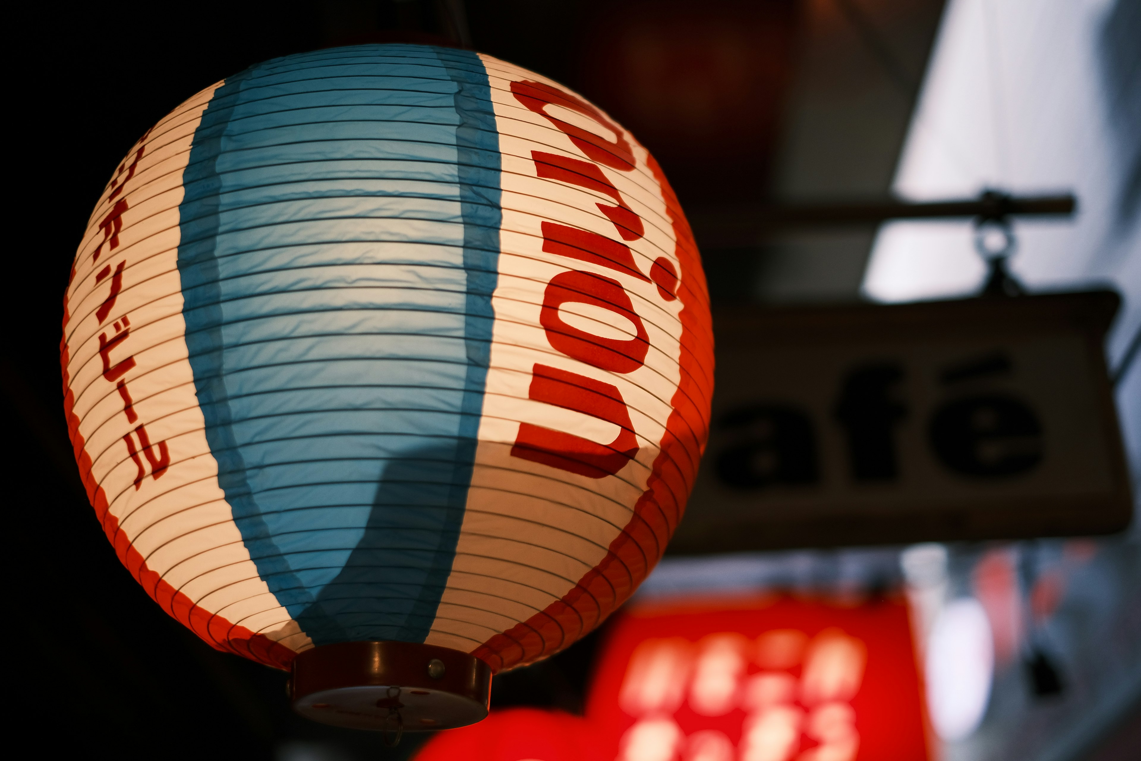 Linterna a rayas rojas y azules colgando frente a un cartel de café