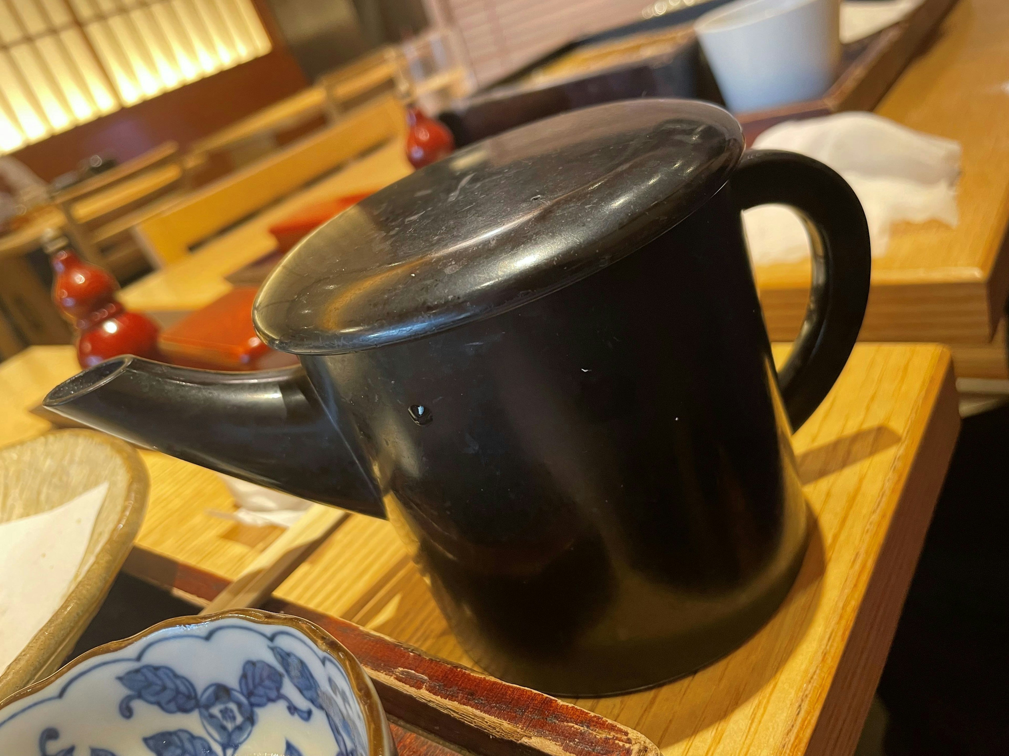 A black teapot placed on a table in a Japanese-style restaurant interior