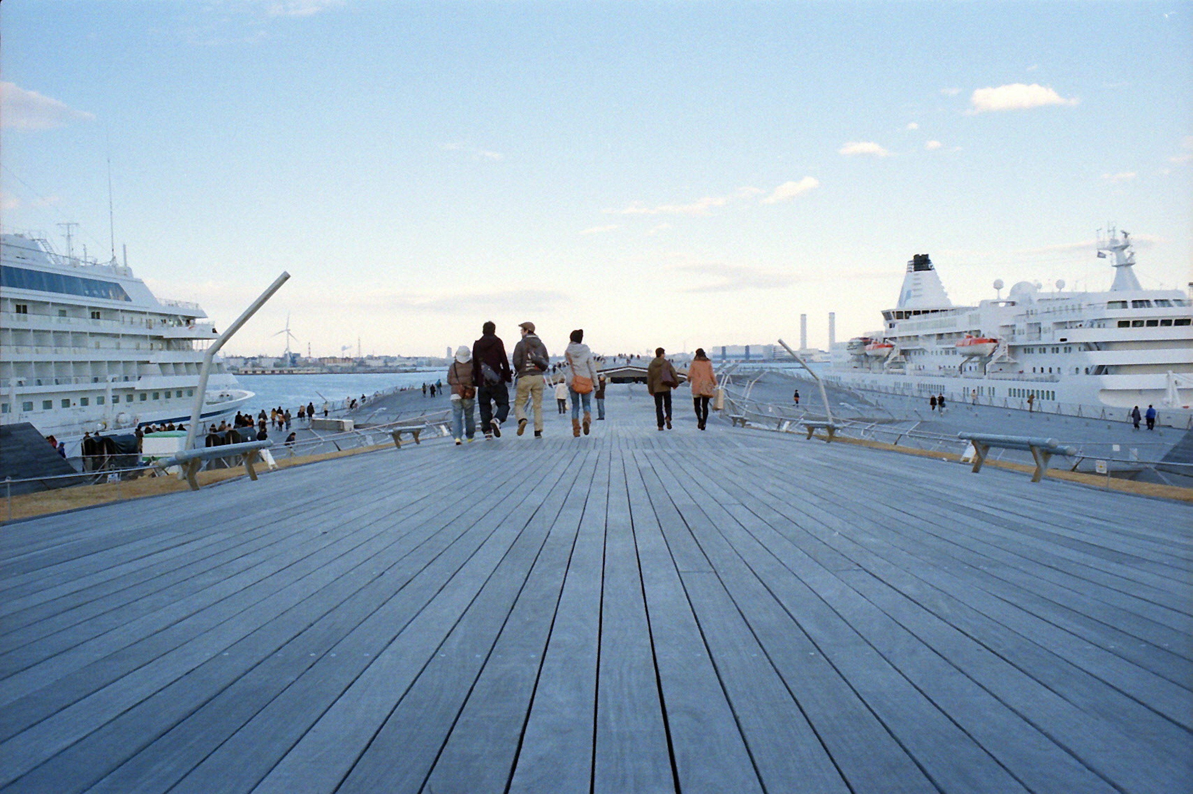 People walking on a pier under a blue sky with boats