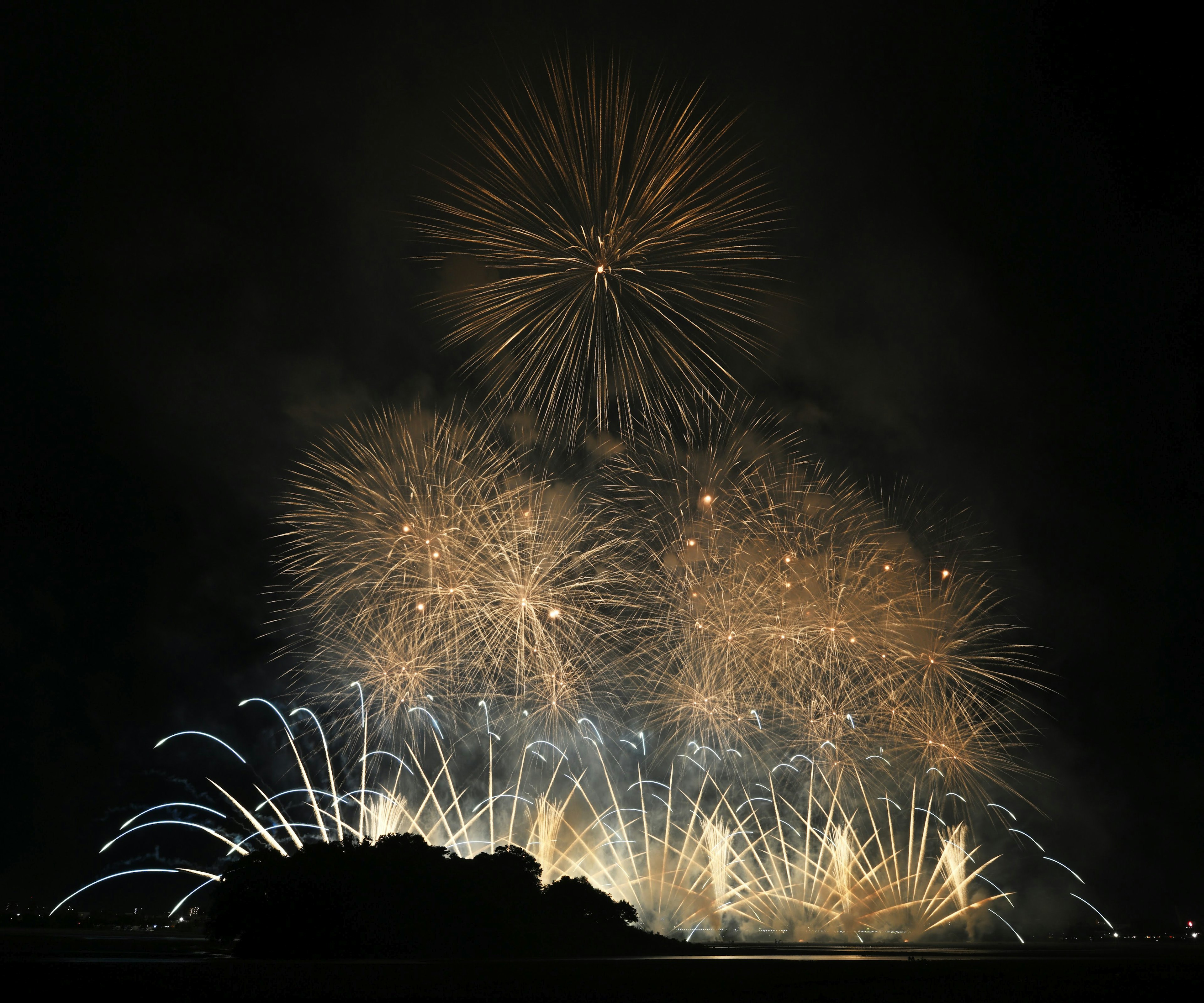 Espectáculo de fuegos artificiales iluminando el cielo nocturno con explosiones de luz dorada y una isla en silueta al fondo