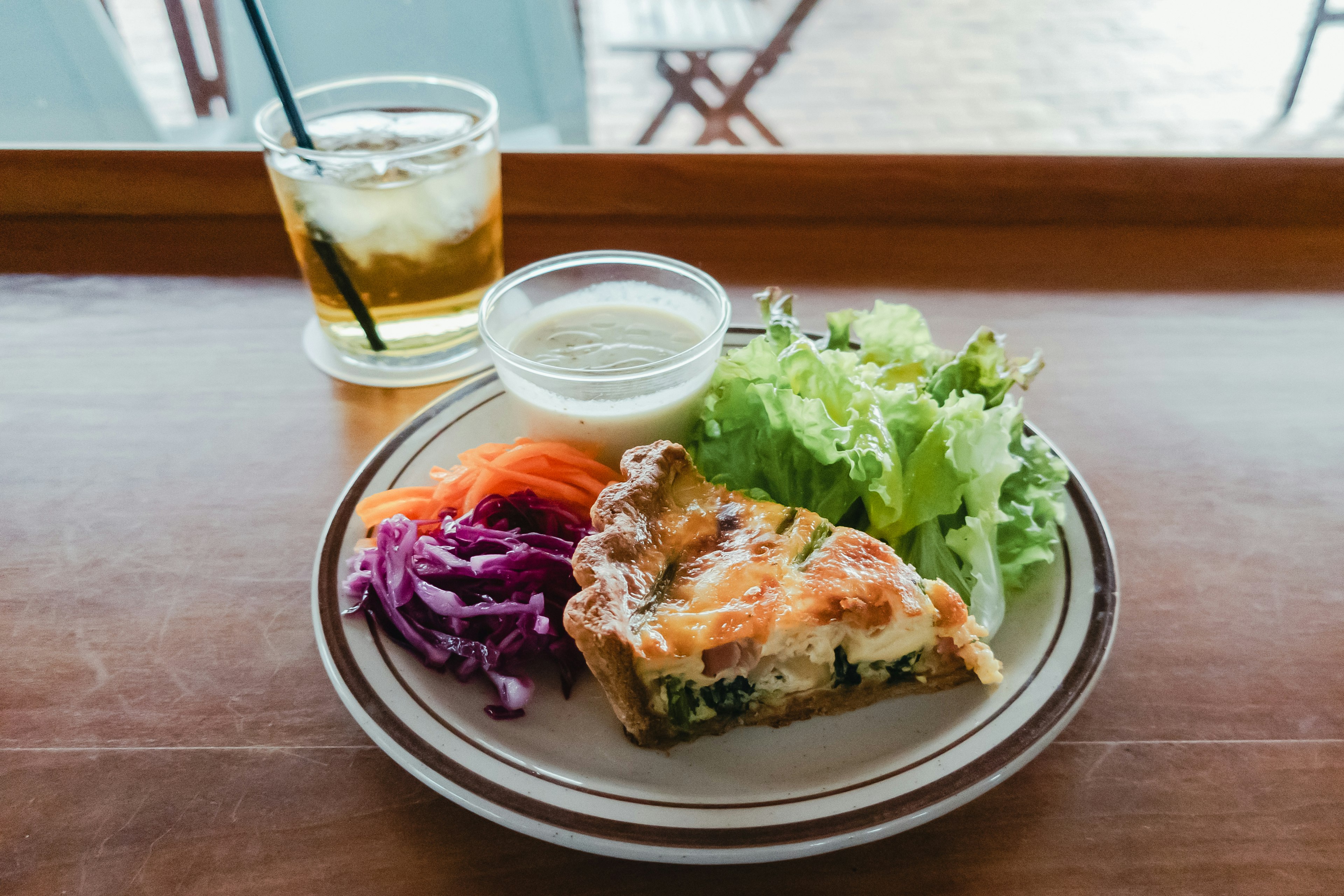 Một đĩa có bánh quiche, salad và nước chấm trên bàn gỗ