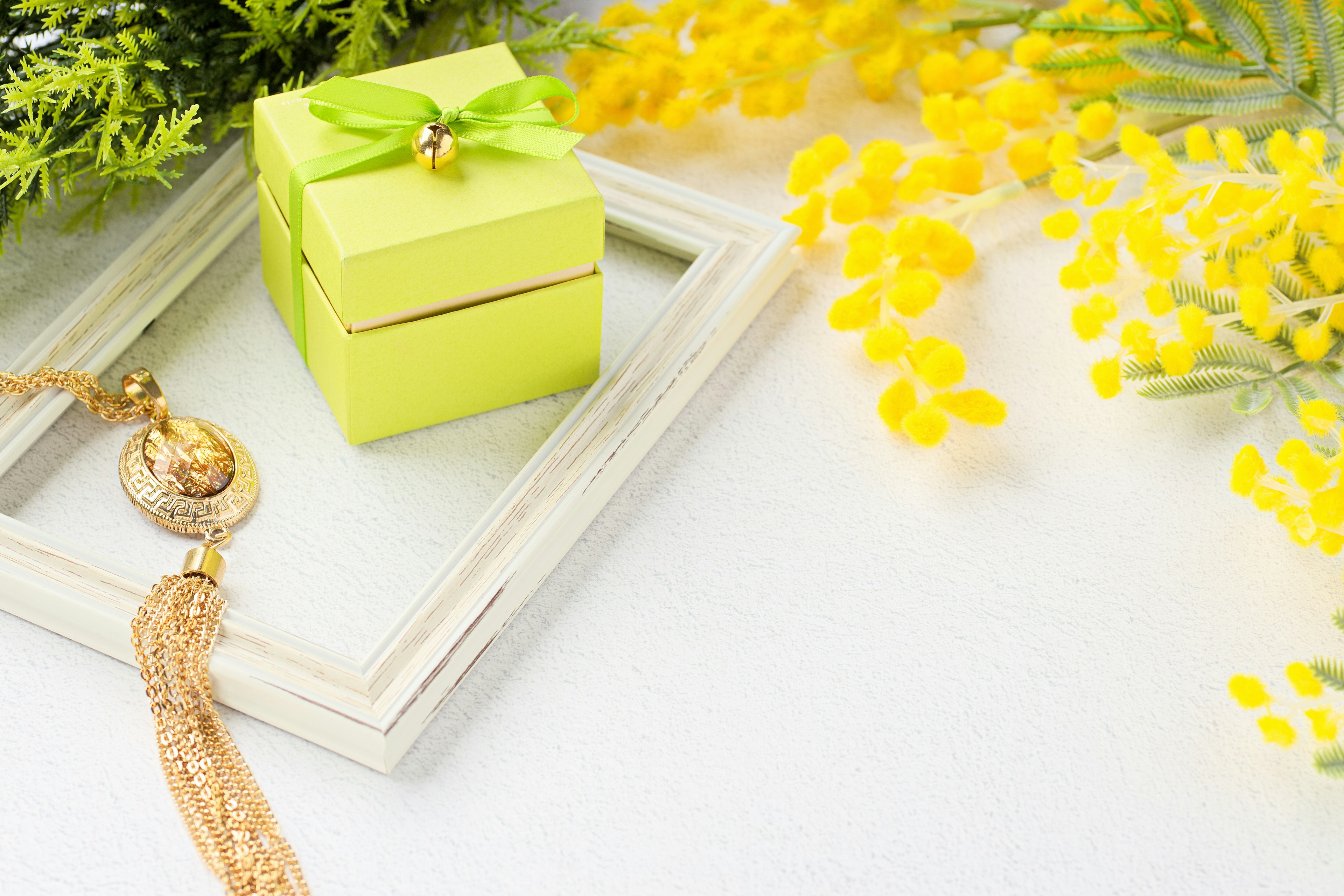 A green gift box with a bow next to yellow flowers and a decorative frame