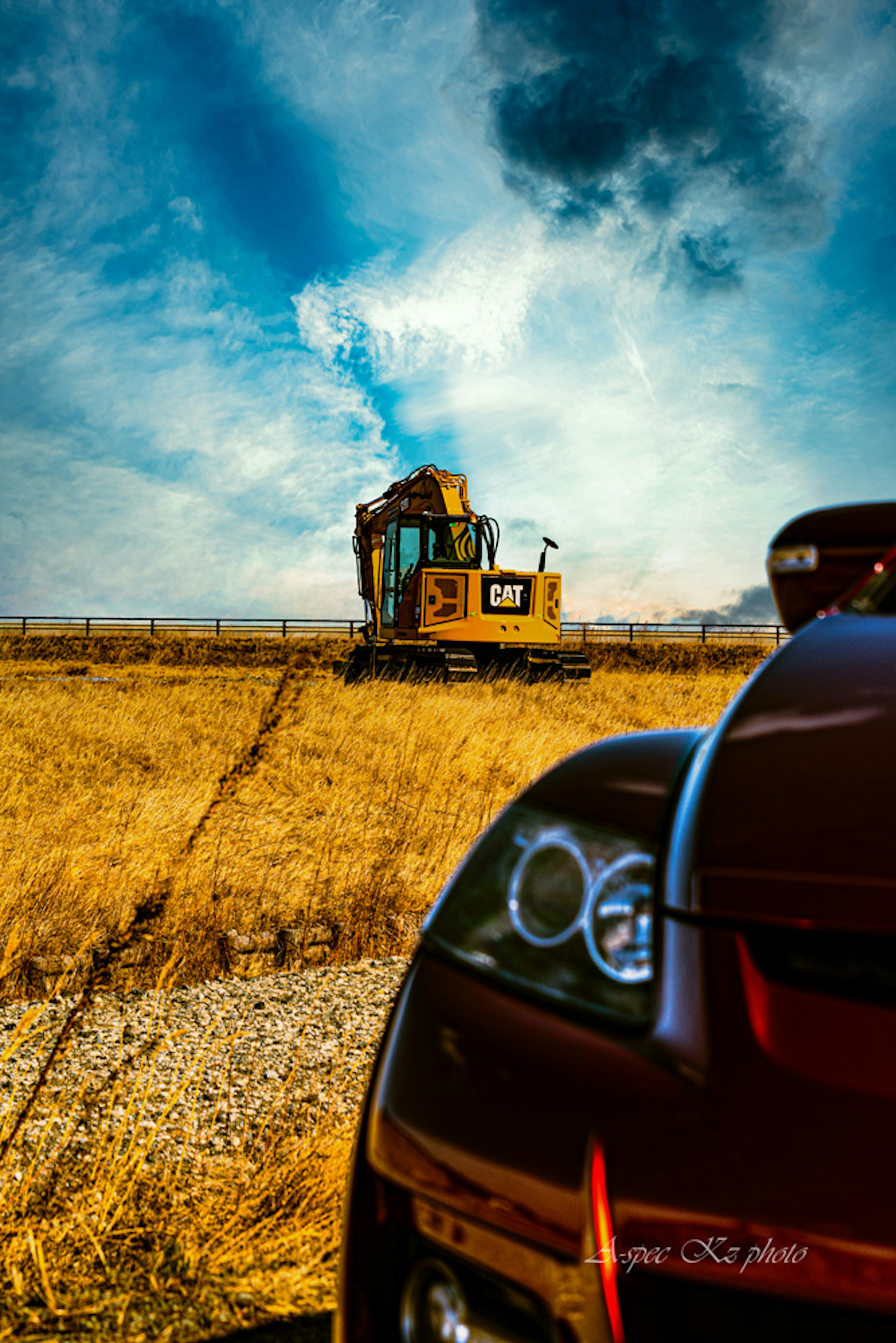 Un coche rojo en primer plano y un vehículo de construcción amarillo trabajando en un vasto campo