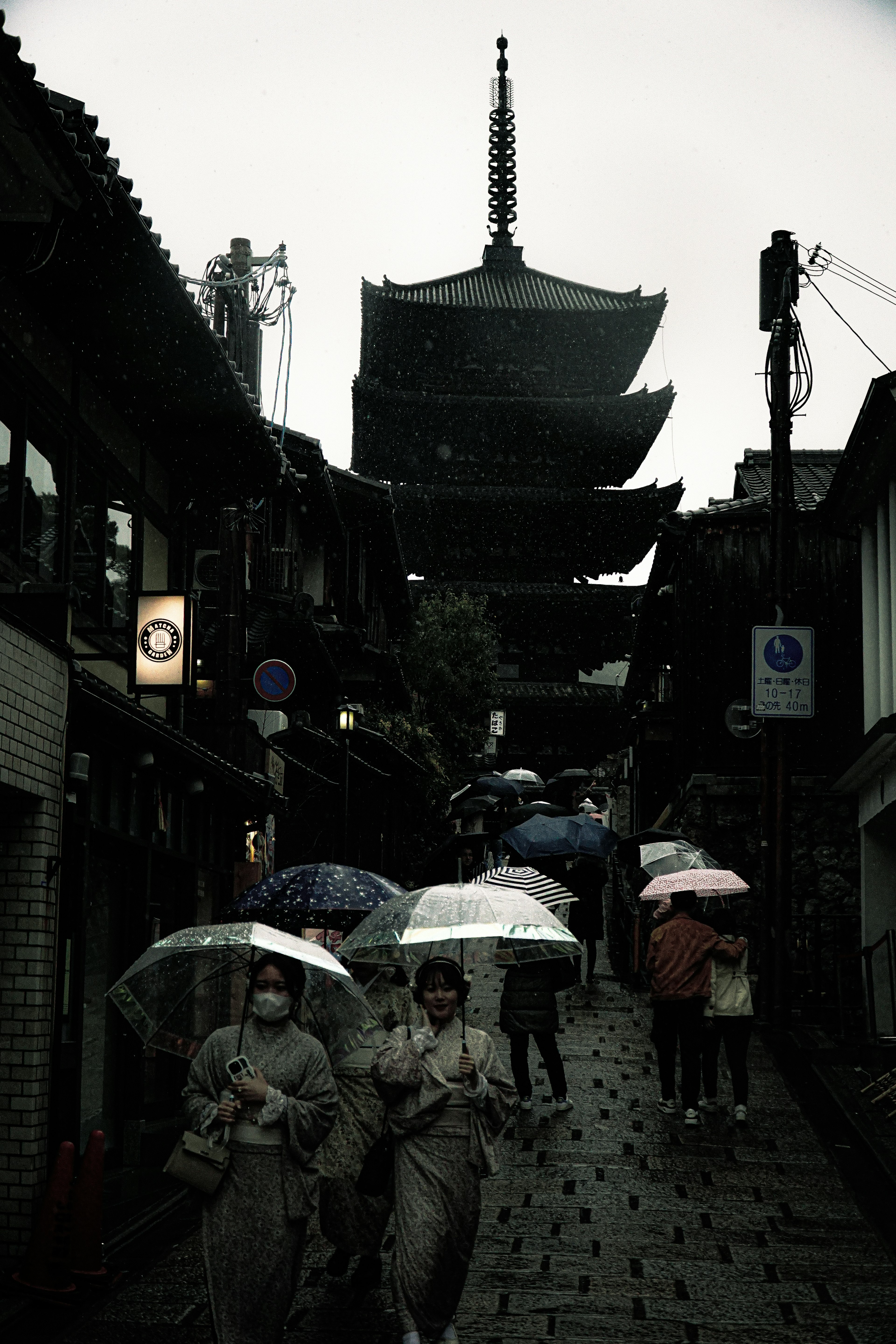 Escena de calle con personas en kimonos y una pagoda bajo la lluvia