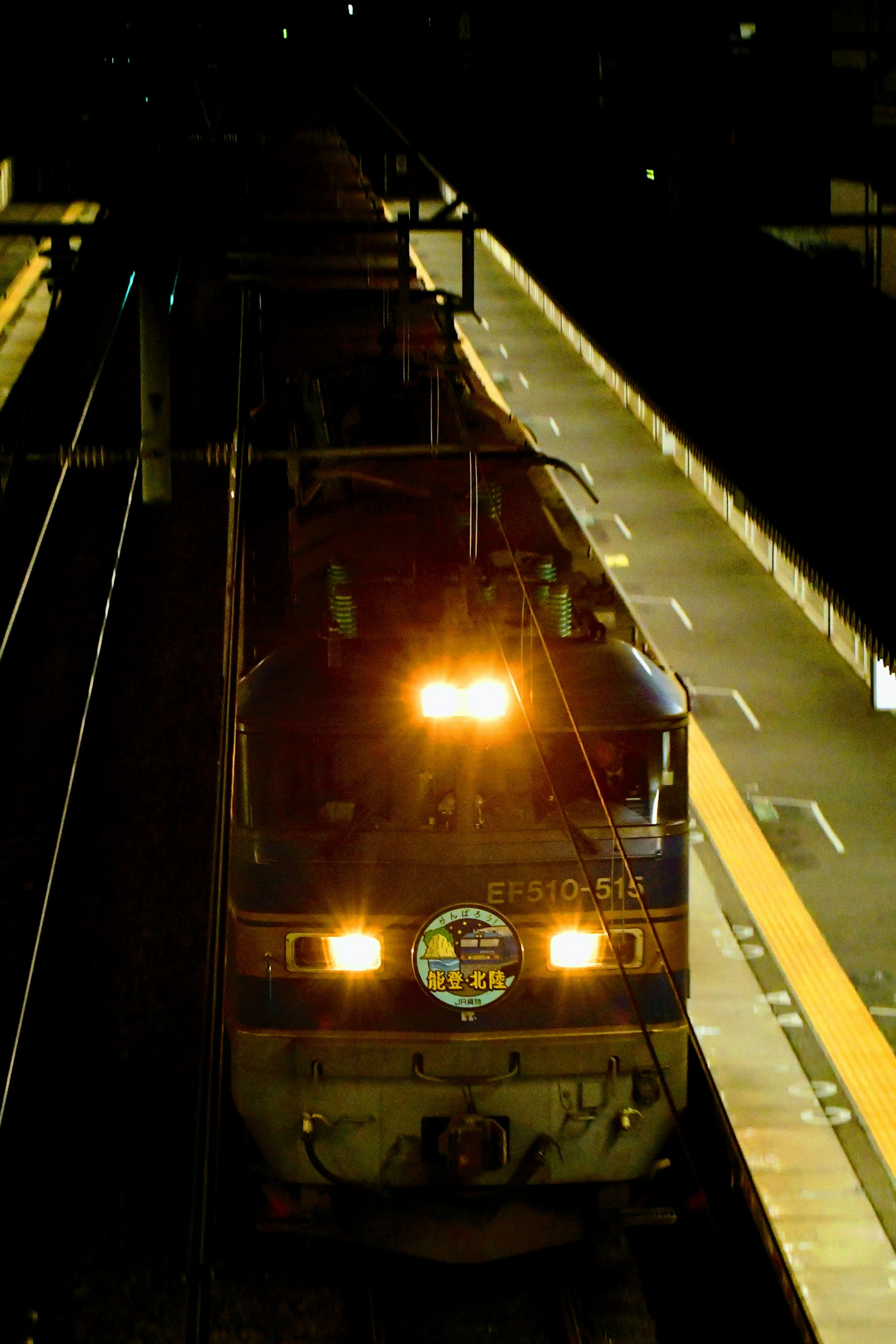 Freight train stopped at a station at night bright headlights and visible platform