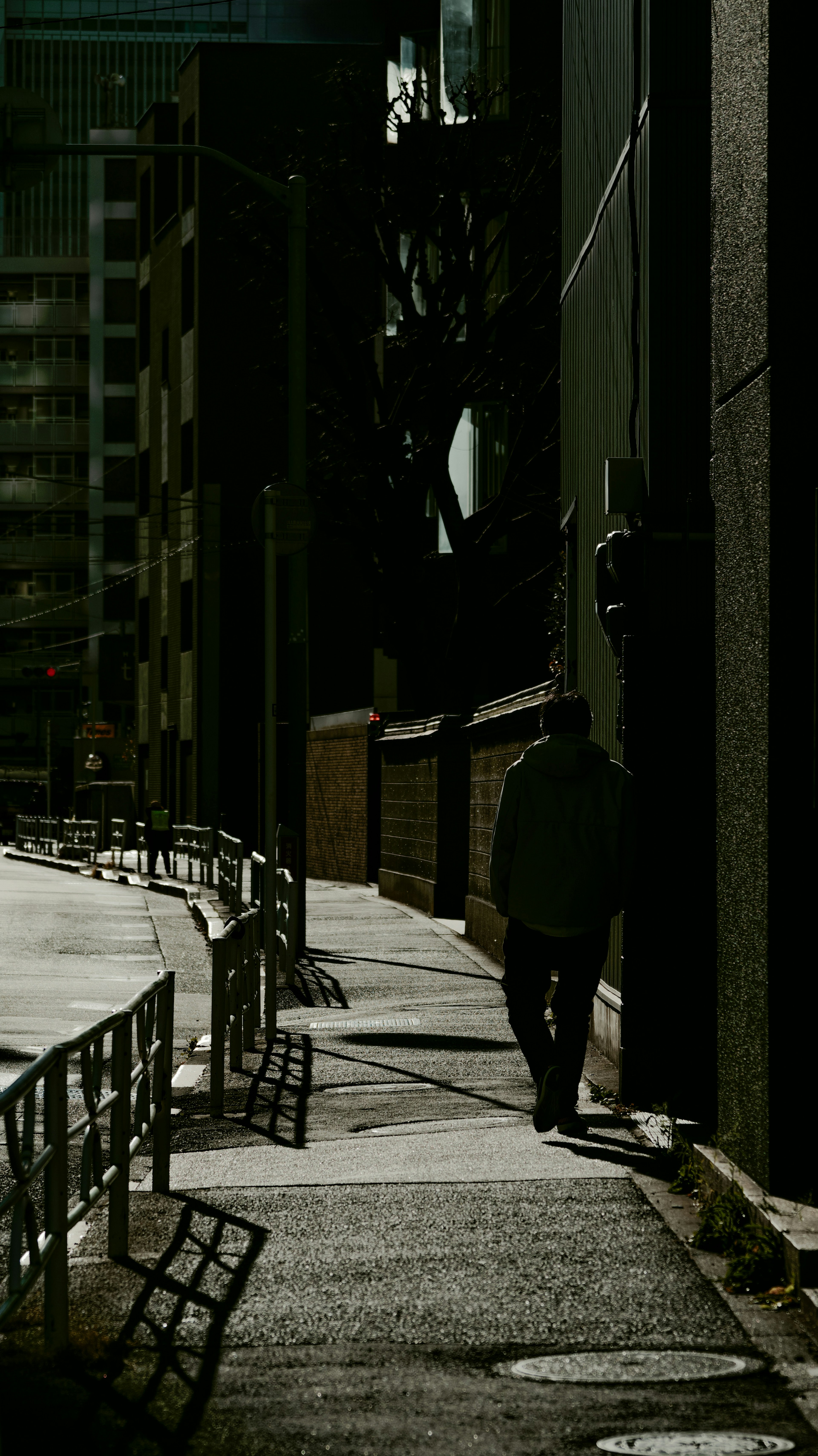 Silhouette d'une personne marchant dans une rue sombre avec des ombres de bâtiments