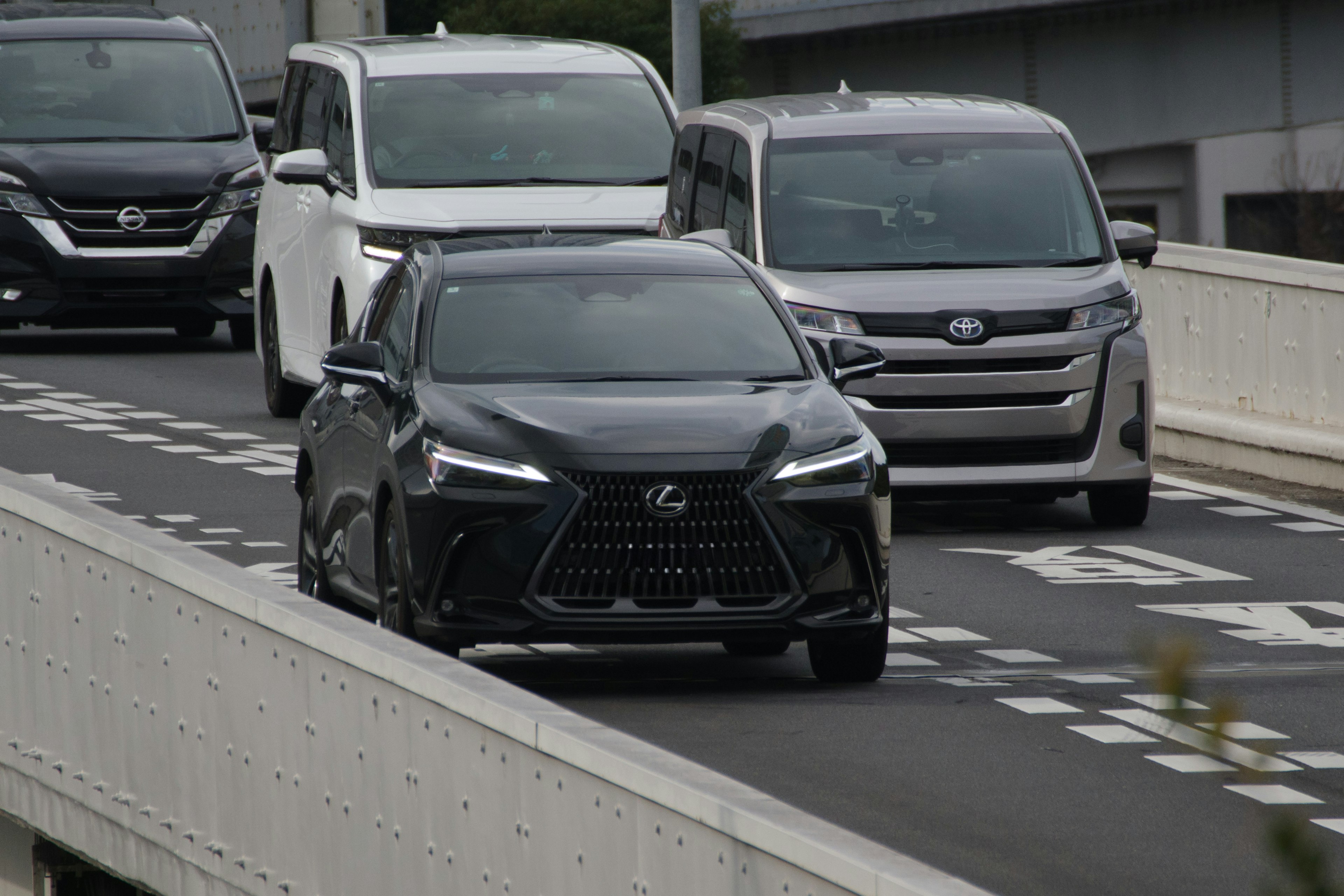 Une voiture Lexus noire roulant sur une autoroute avec des véhicules blancs en arrière-plan