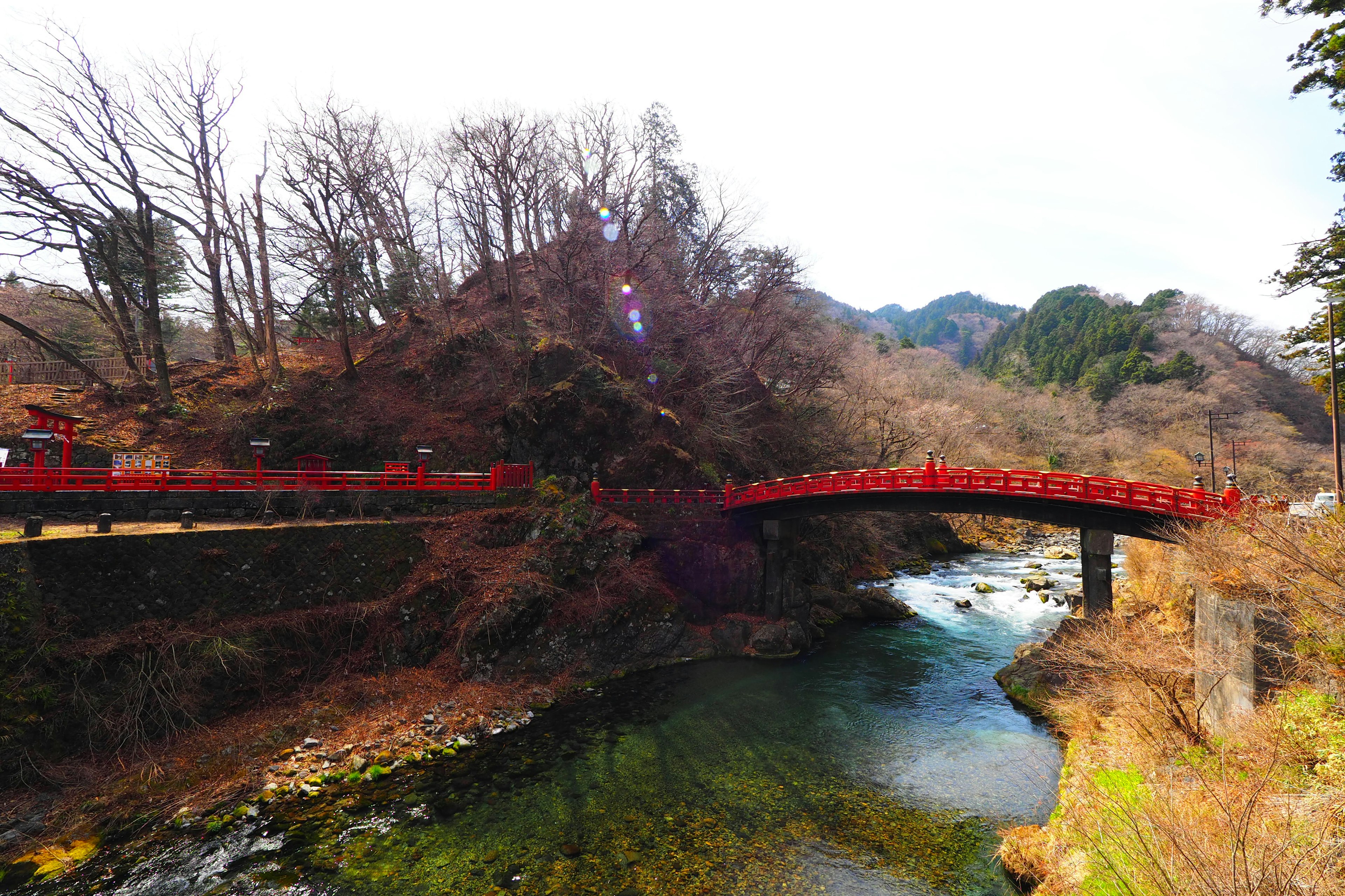 Puente rojo que cruza un río rodeado de árboles de invierno y montañas