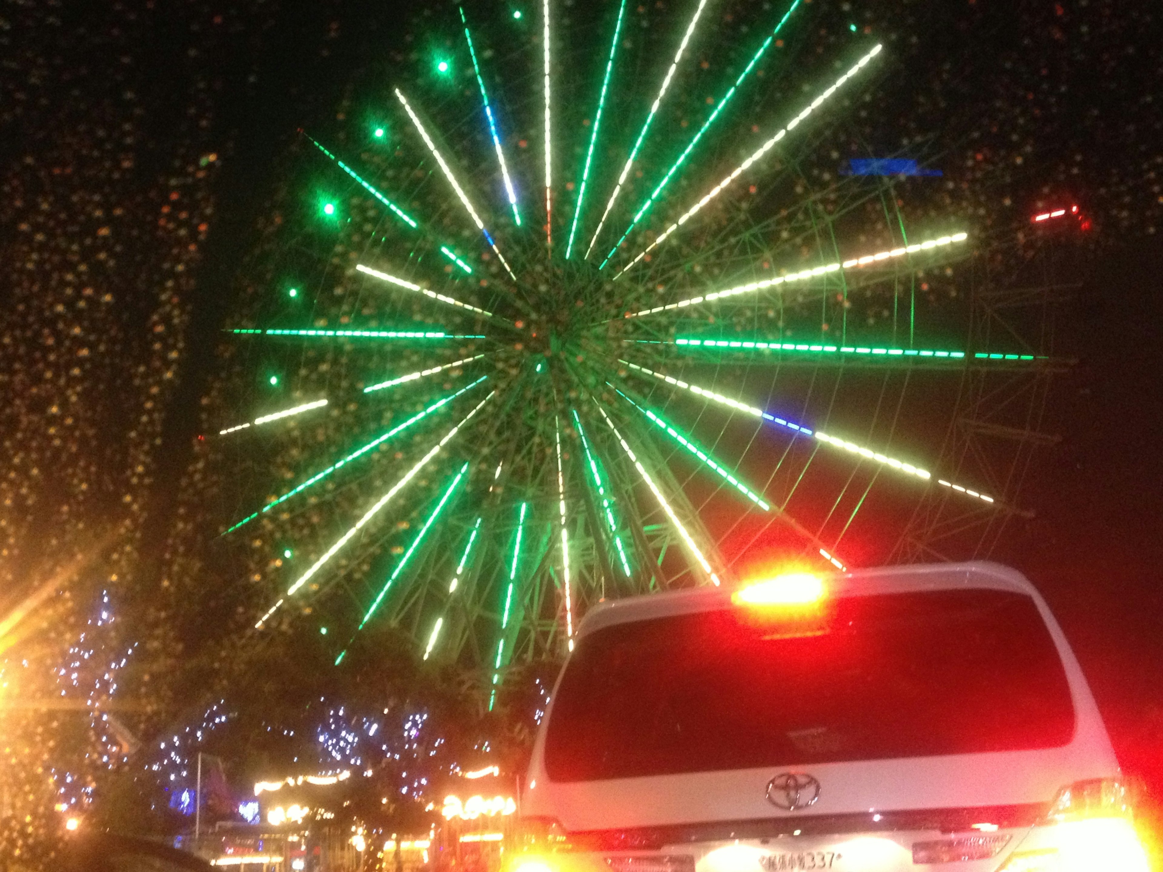 Night view of a green illuminated Ferris wheel and car tail lights