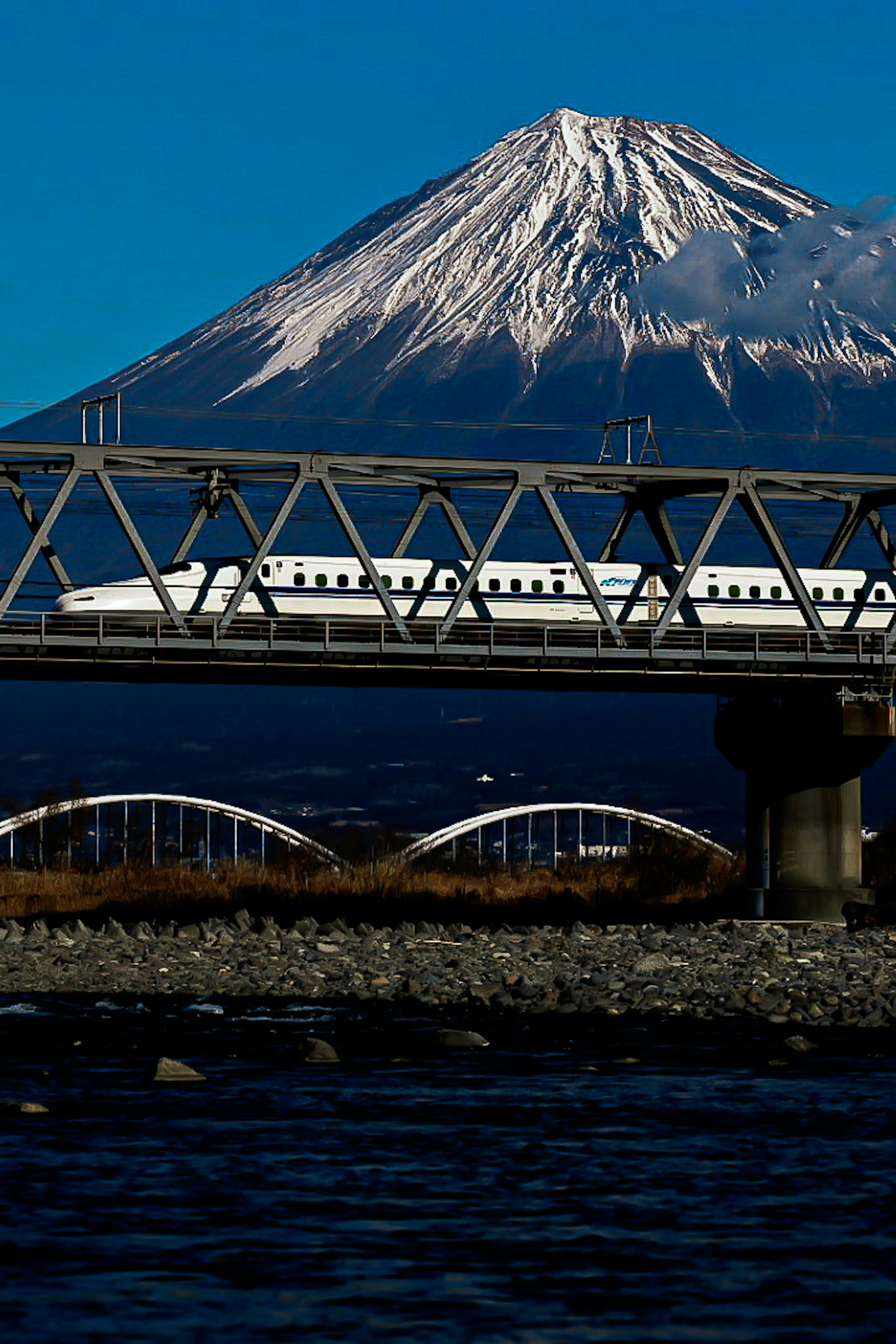 Snow-capped Mount Fuji with a train crossing a bridge