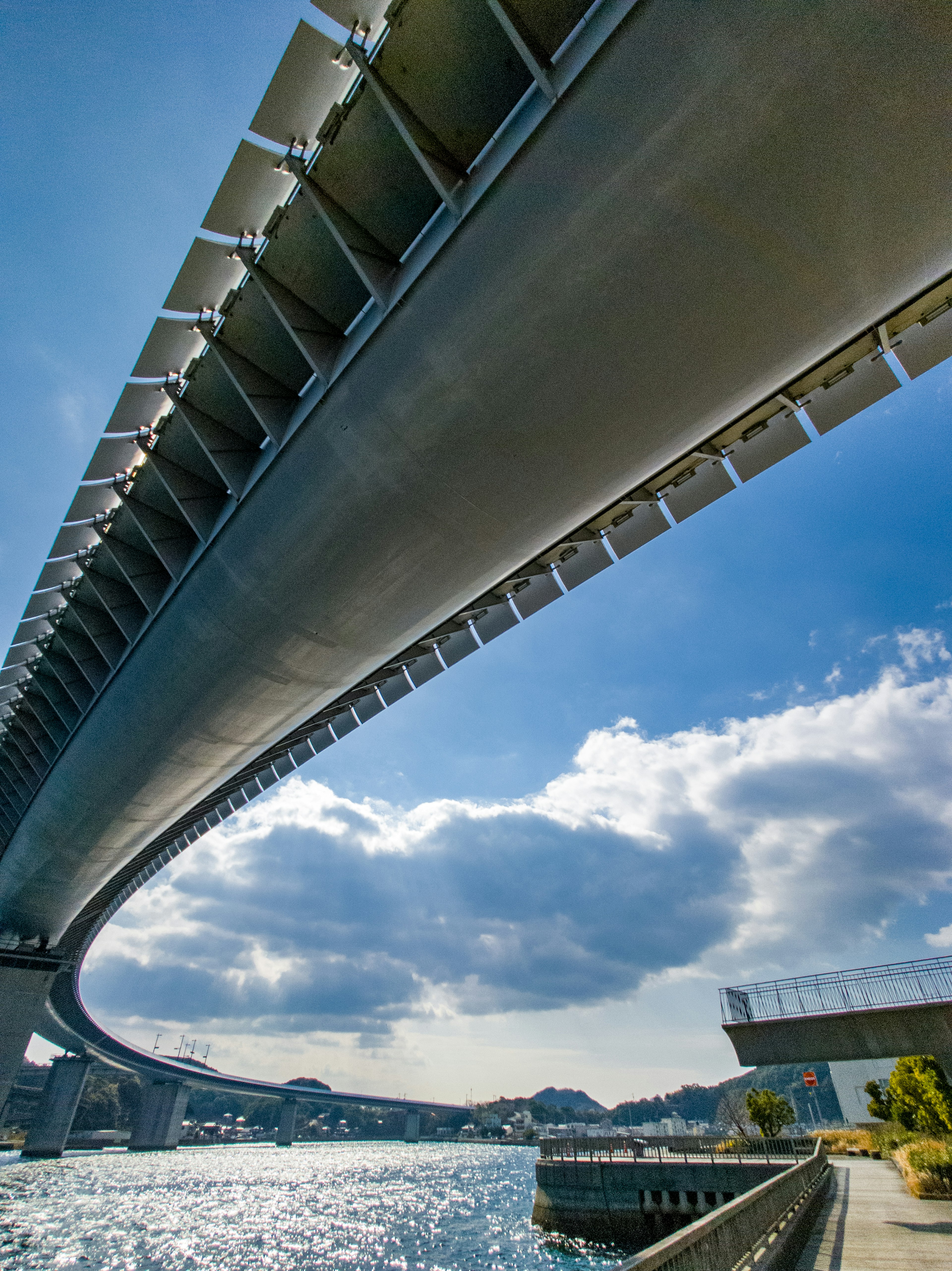 Vista desde abajo de un puente moderno que cruza un río Cielo azul brillante con nubes blancas de fondo