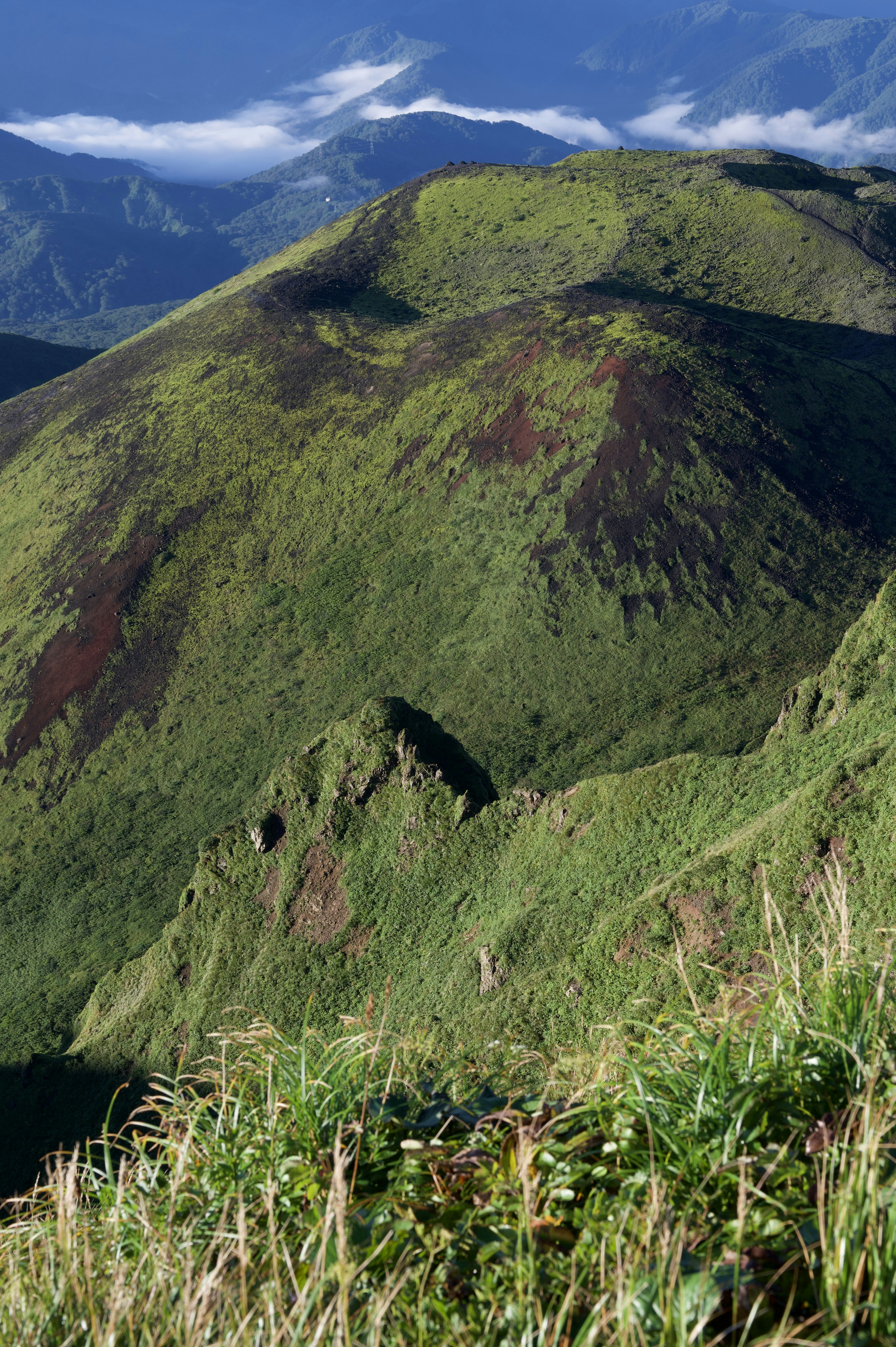 Lush green mountainside with blue sky and clouds