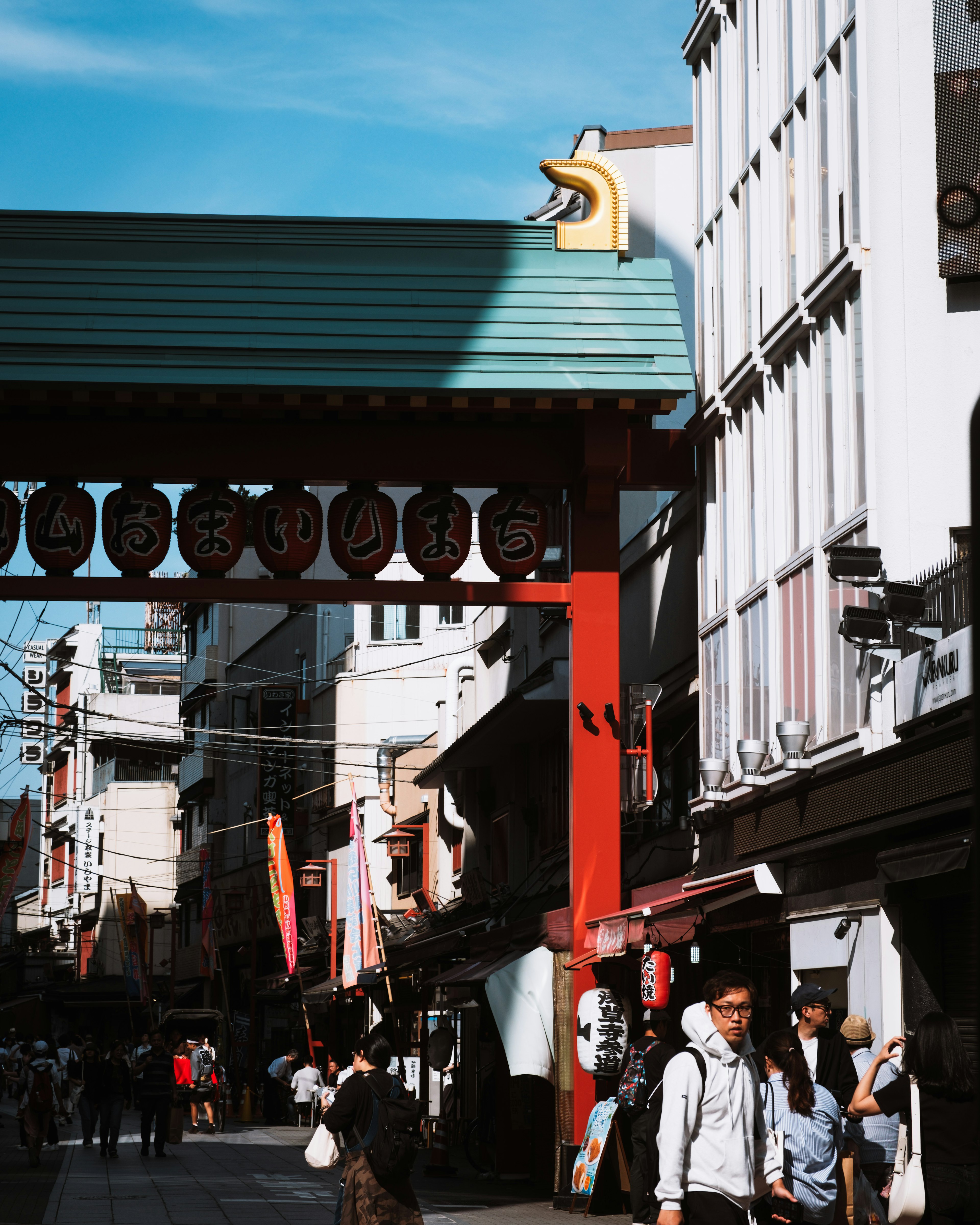 Busy street with people walking under a red gate and blue sky