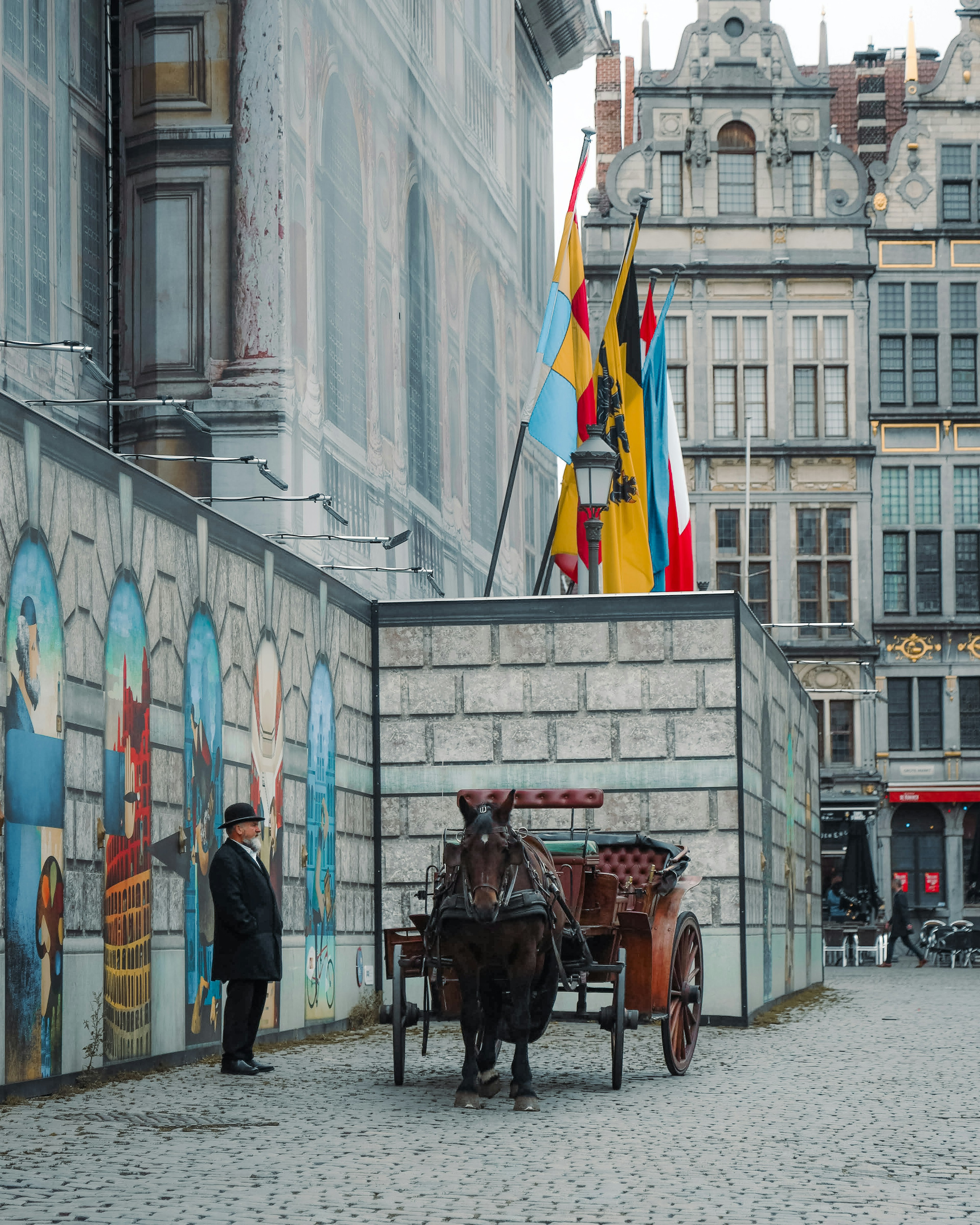 A horse-drawn carriage with a man standing near a painted wall in a historical setting