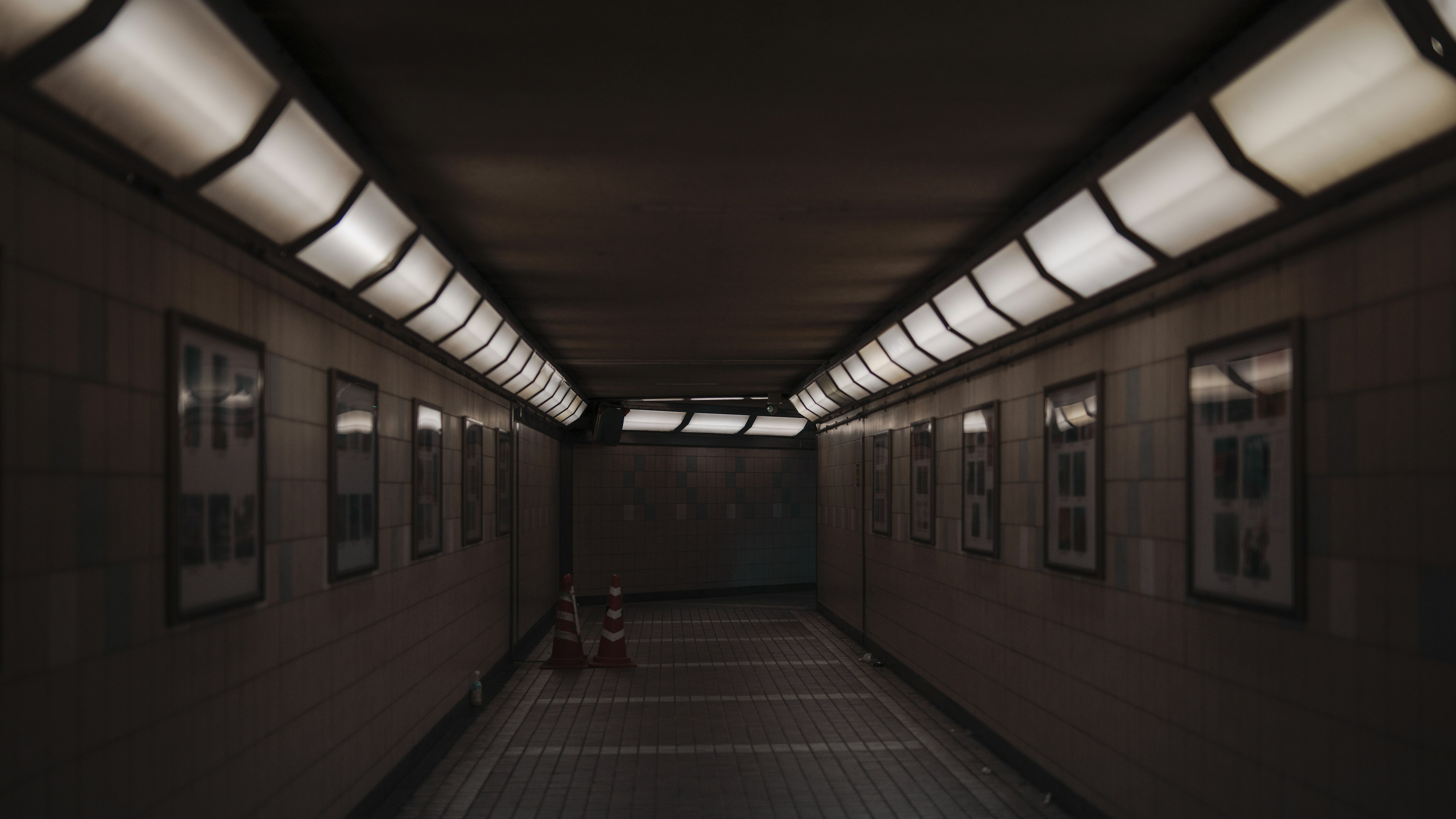 Dimly lit underground corridor with white lights and framed photos on the walls