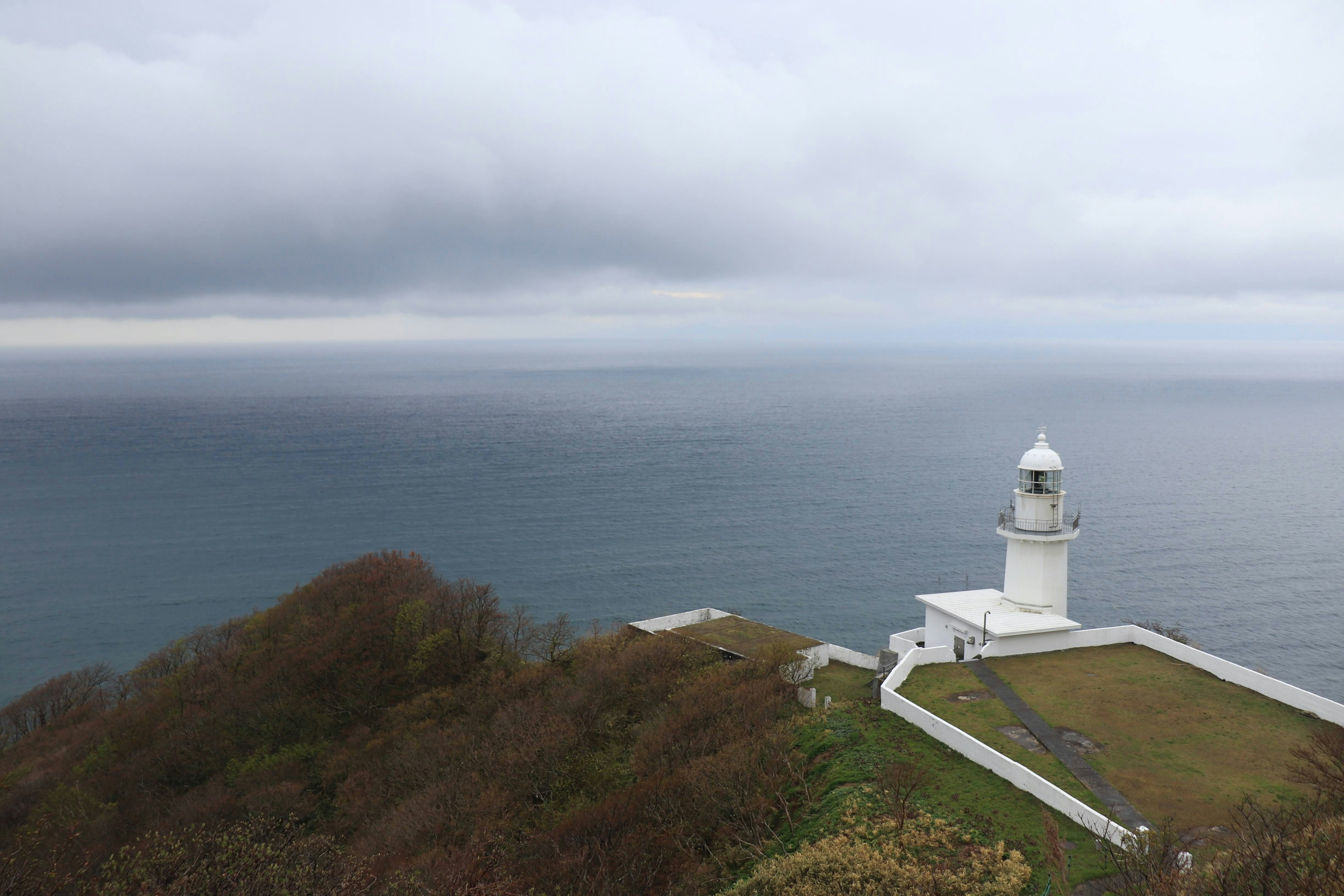 Faro bianco che si affaccia sull'oceano con cielo nuvoloso