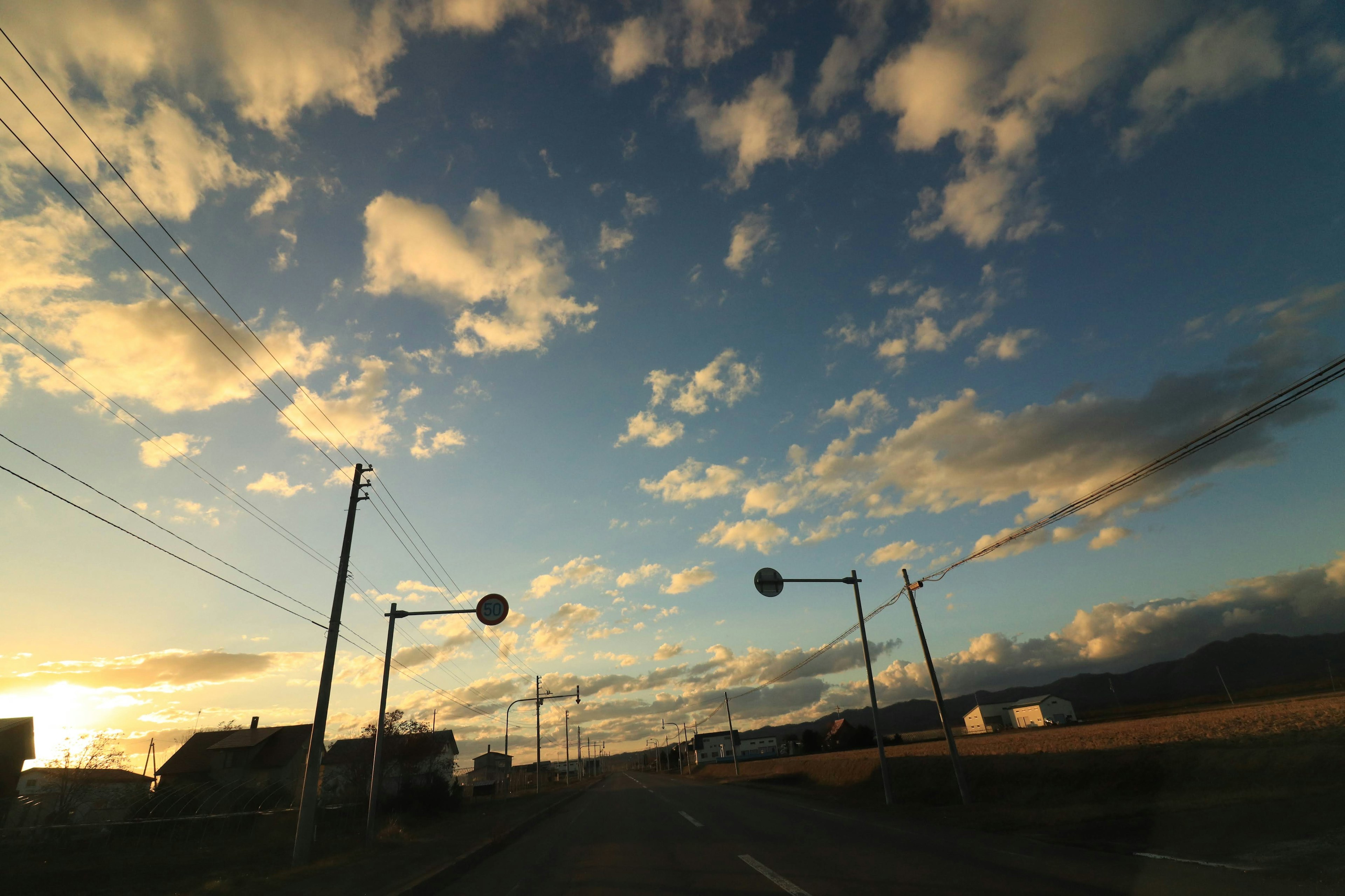 Eine malerische Aussicht auf einen blauen Himmel mit Wolken während des Sonnenuntergangs mit einer Straße und Verkehrszeichen