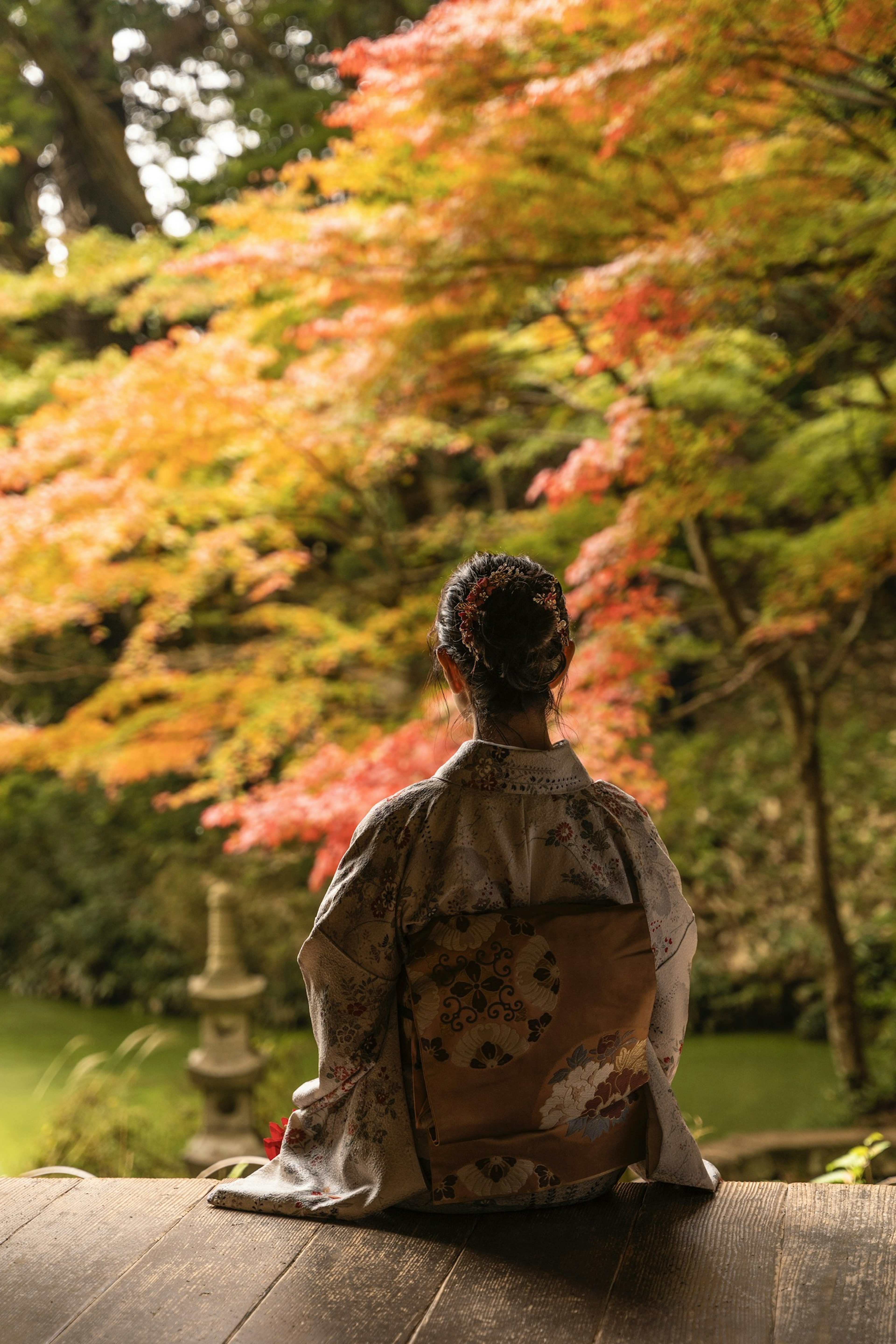 Seorang wanita berpakaian kimono duduk di taman dengan dedaunan musim gugur yang indah