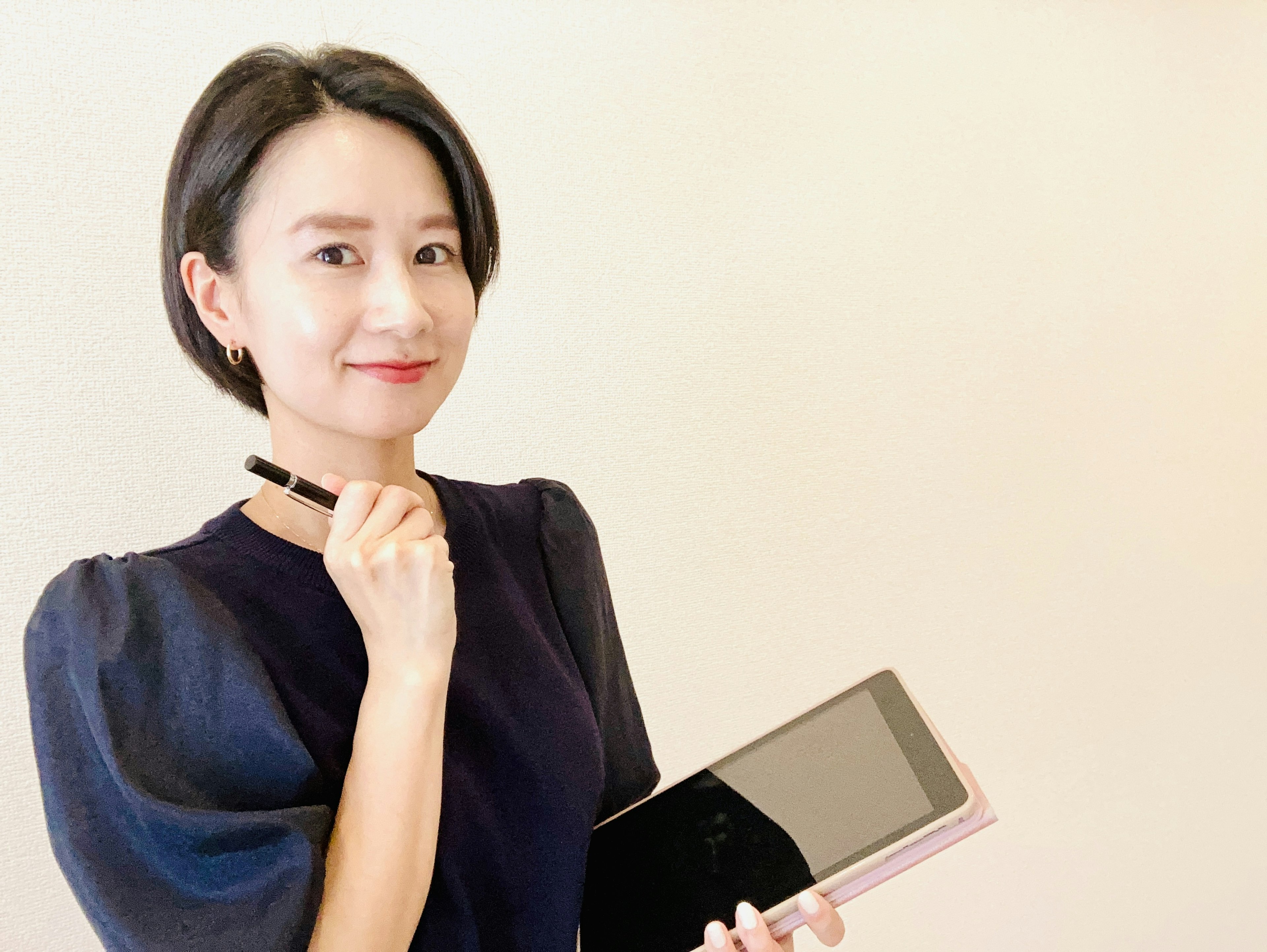 A woman smiling while holding a tablet and a pen