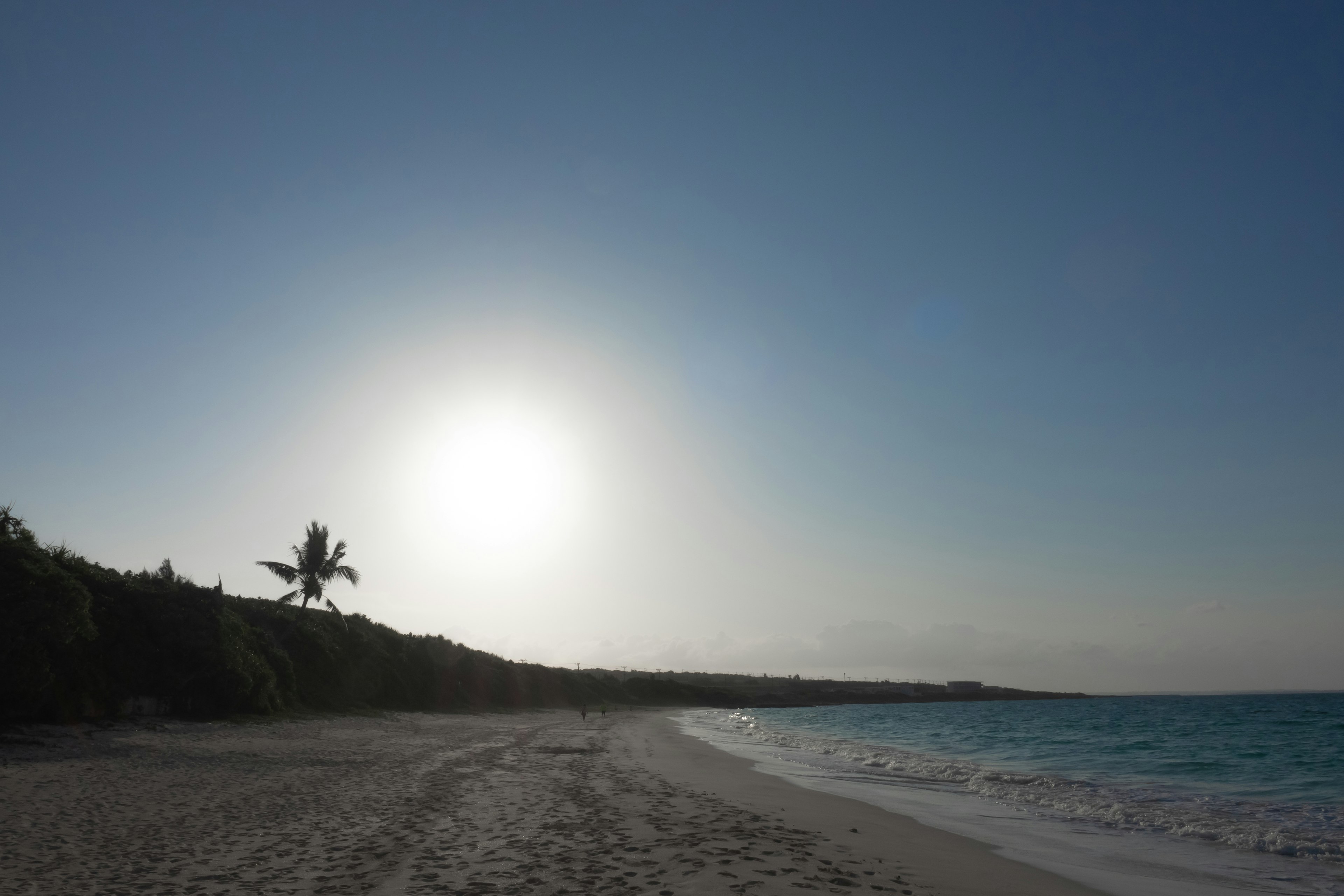 Vue panoramique d'une plage avec mer bleue et sable blanc sous un soleil éclatant