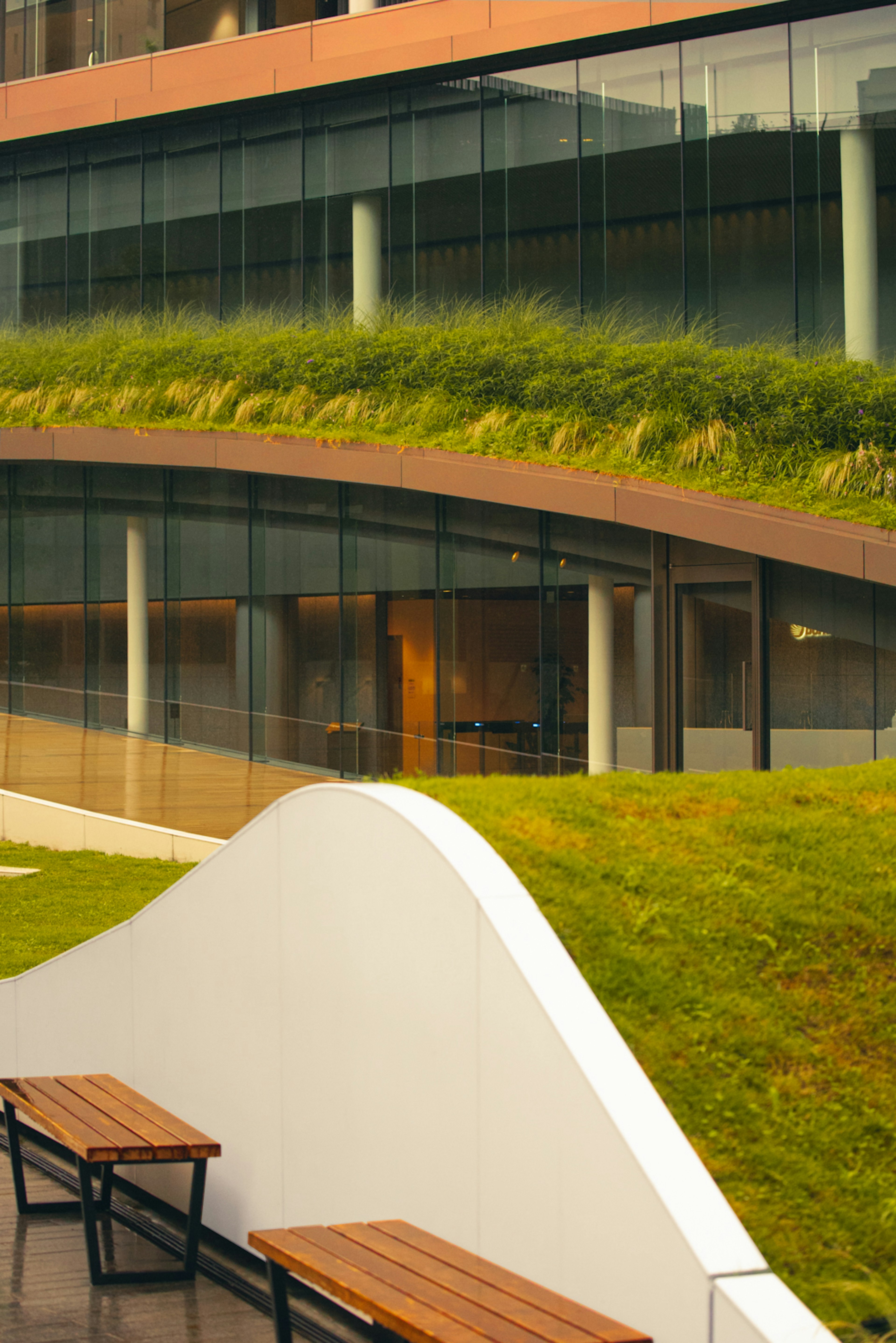 Partie d'un bâtiment moderne avec un toit vert et un banc incurvé blanc